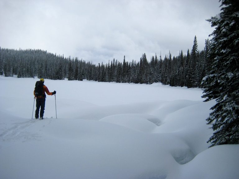 A backcountry skier stands at the edge of frozen Poland Lake below Bojo Mountain