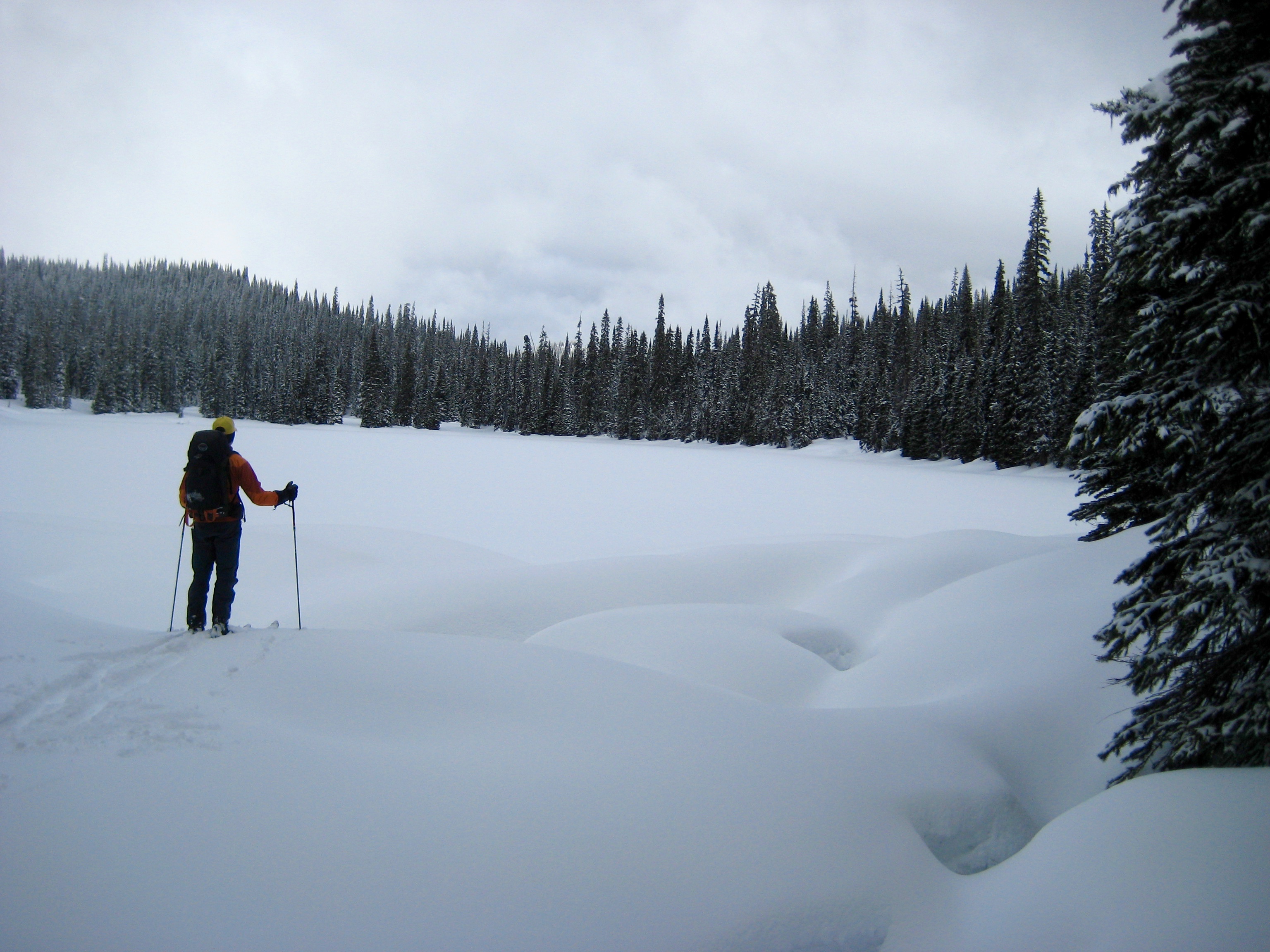 A backcountry skier stands at the edge of frozen Poland Lake below Bojo Mountain