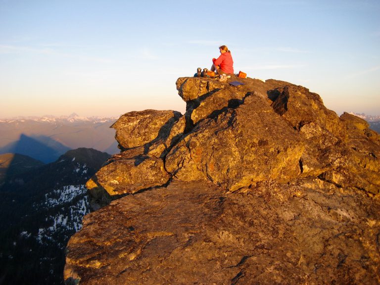 A mountain climber relaxes on summit of Mt Baring in evening alpenglow