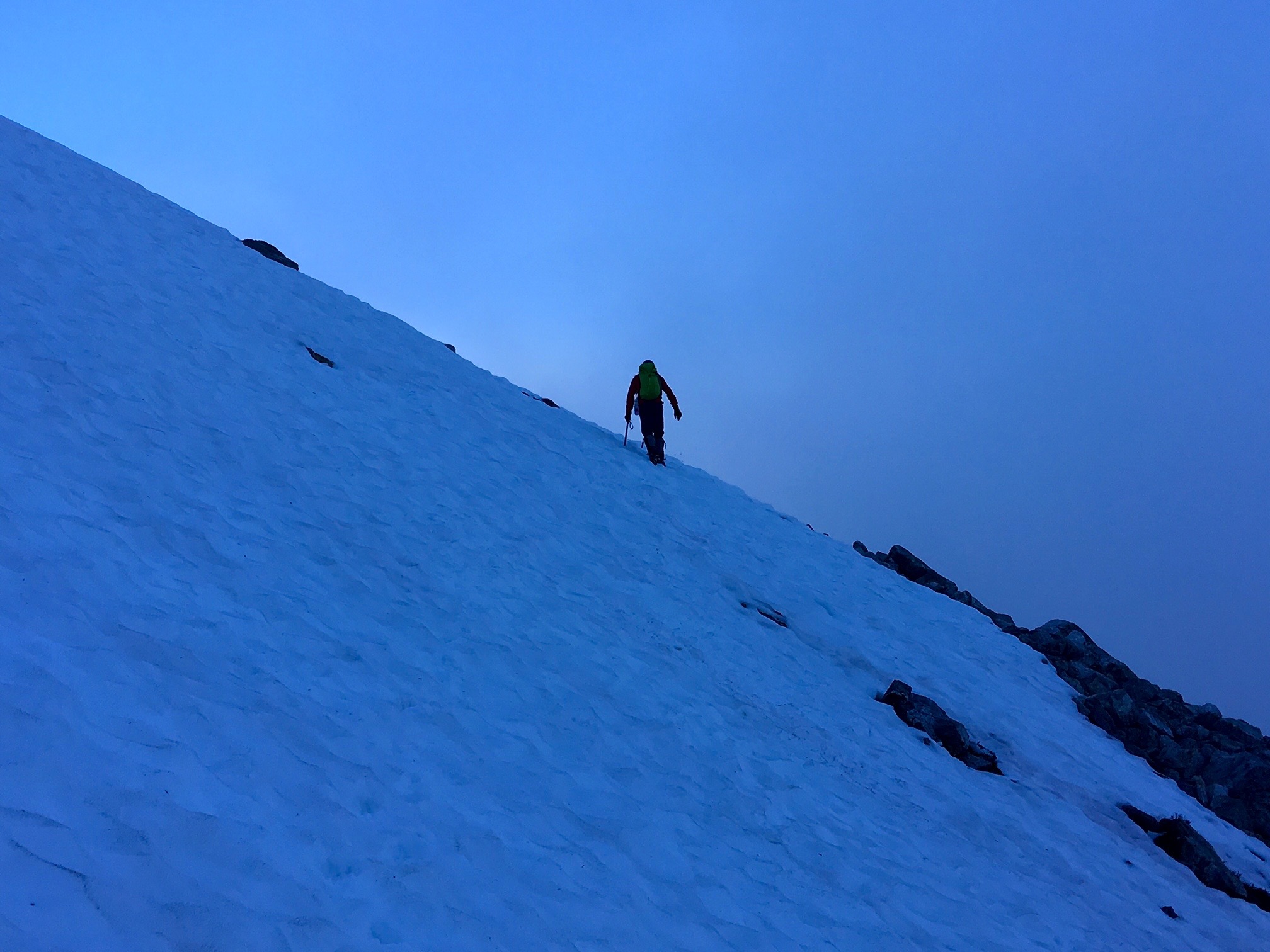 lone mountain climber traversing snow slopes in the blue light before dawn on the way to Phantom Peak