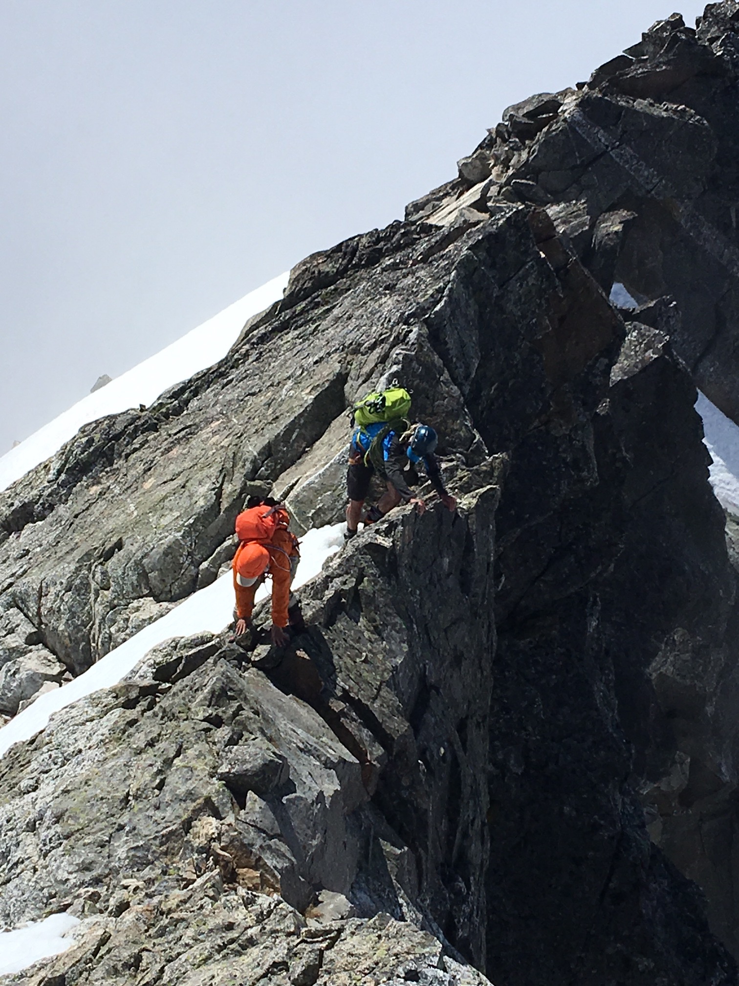 mountain climbers scrambling rocky summit ridge of Phantom Peak with lingering snow fields