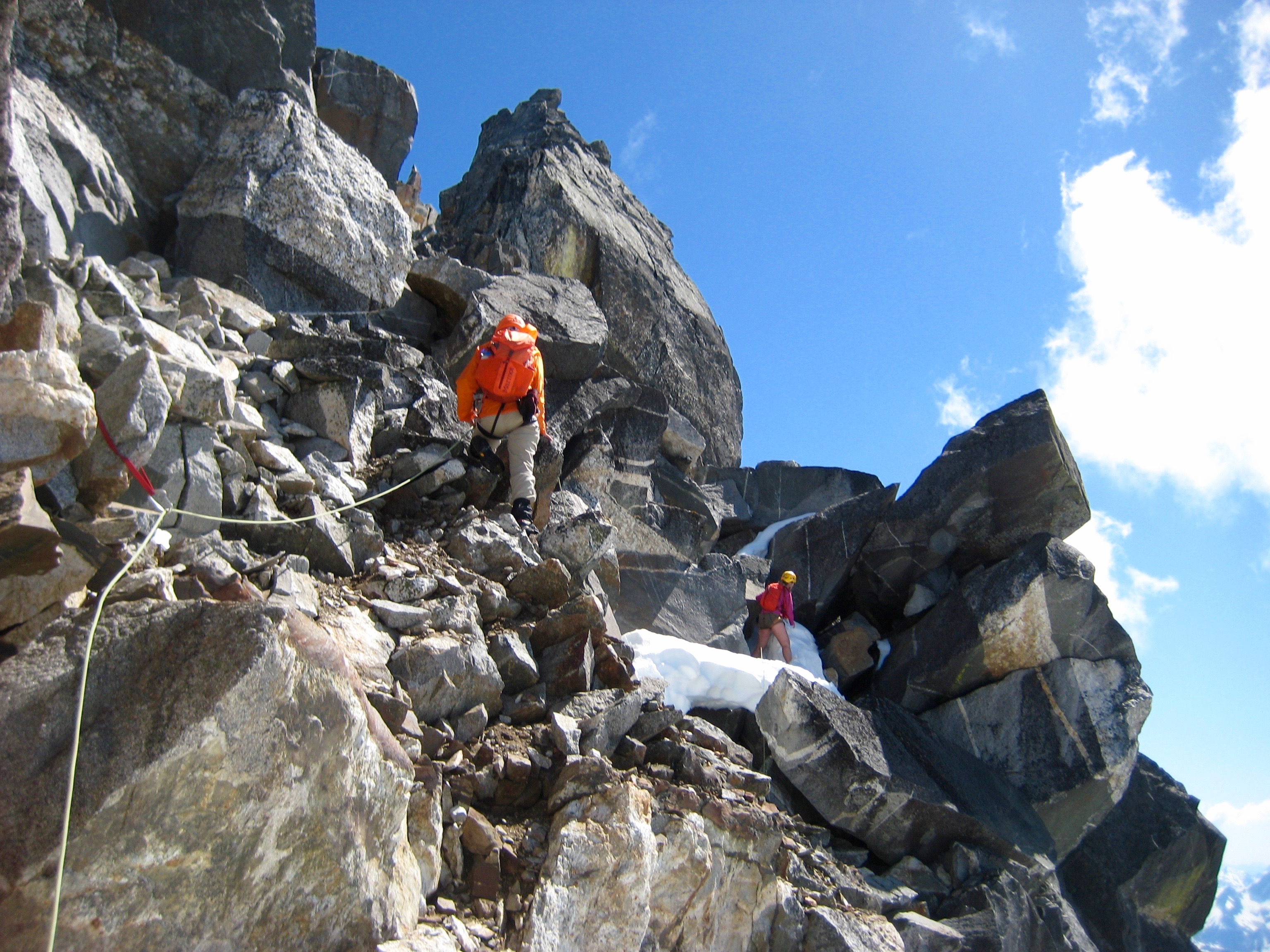 mountain climbers scrambling thru giant boulders and lingering snow patches on the west face of Crooked Thumb Peak