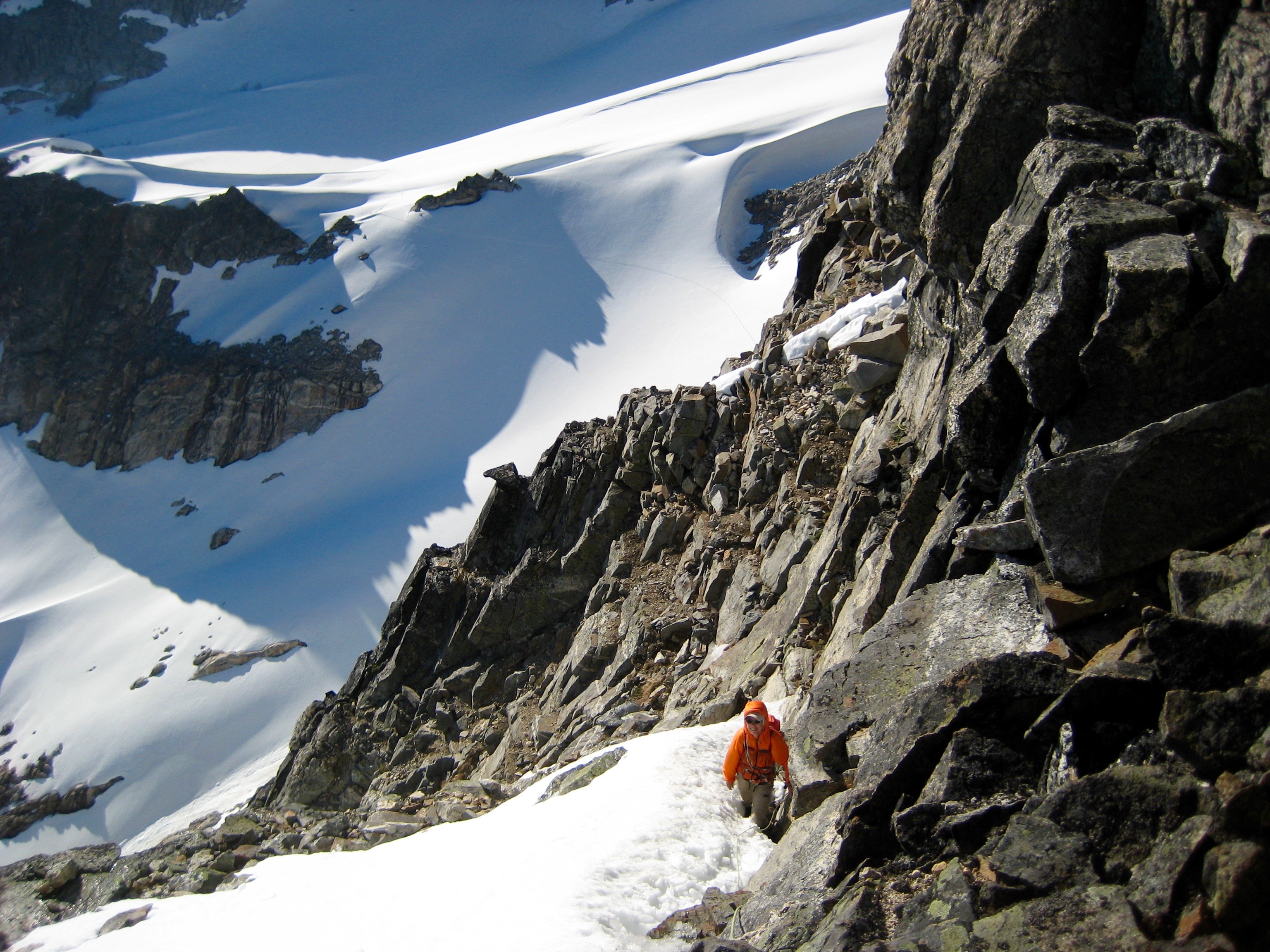 mountain climbers traversing rock ledges and snow patches on the upper west face on Crooked Thumb Peak