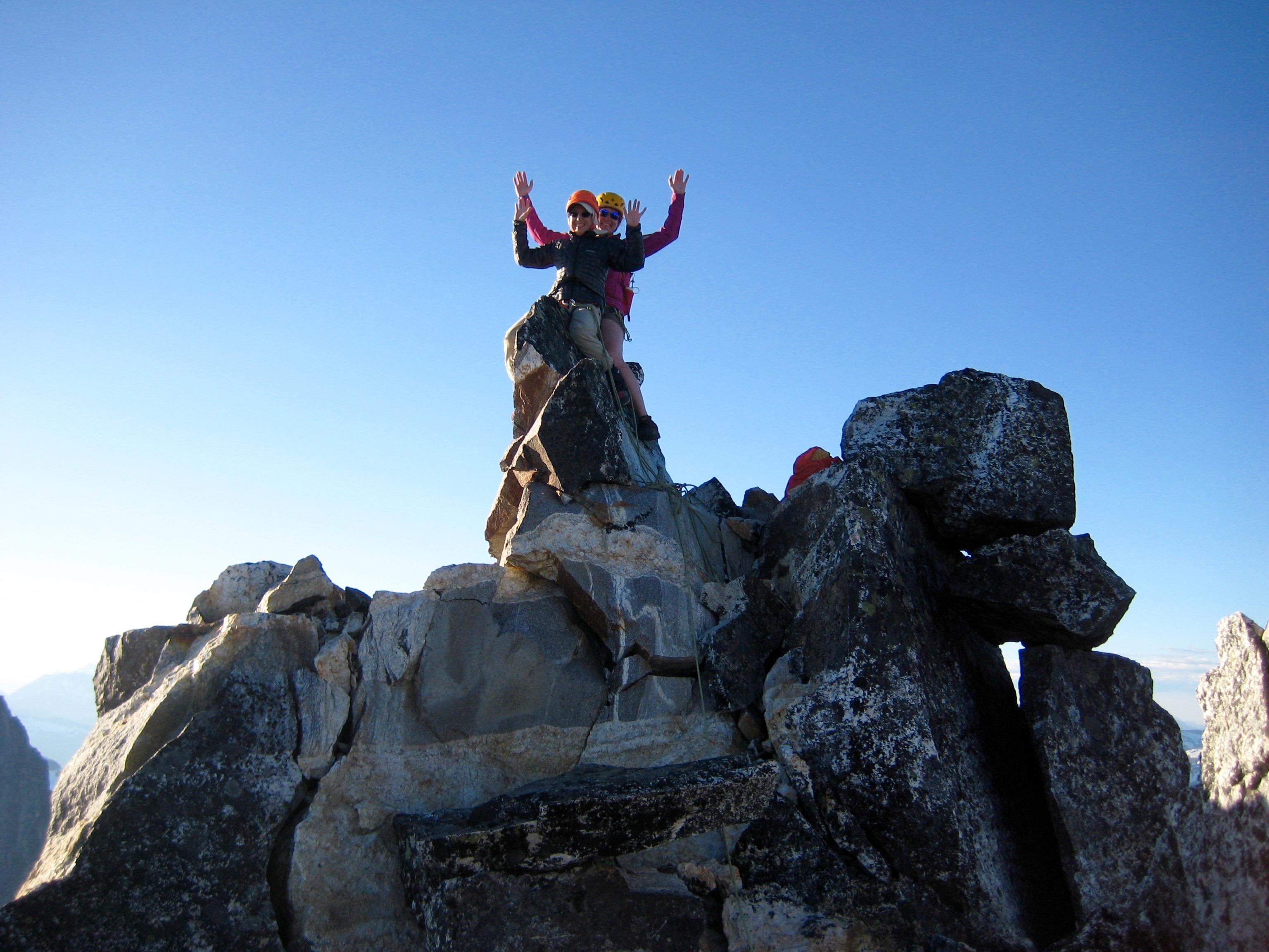 two mountain climbers sitting on the small rocky summit horn of Crooked Thumb Peak in the Picket Range