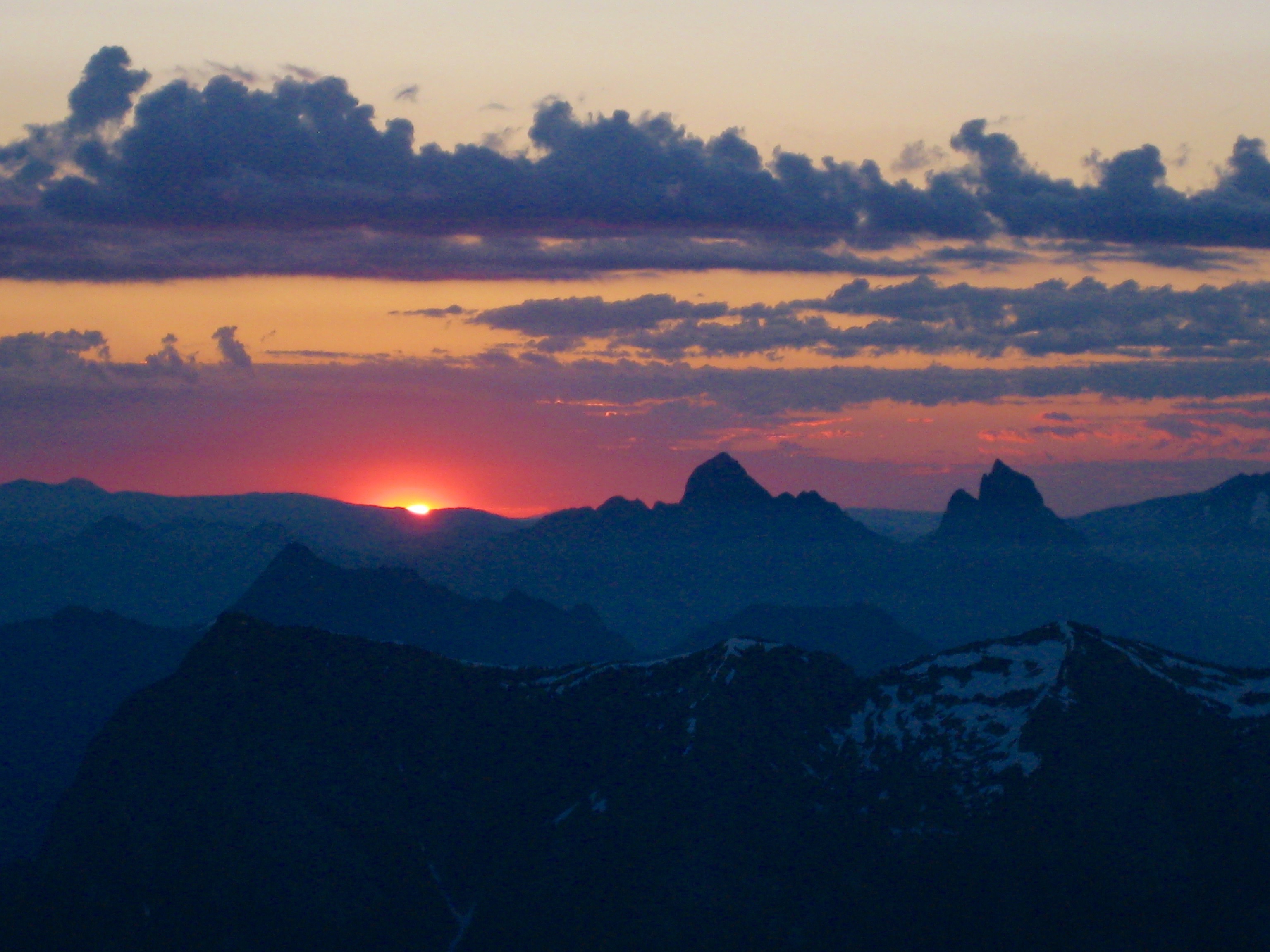 sun breaking the horizon from Crooked Thumb Peak mountain climbing bivouac with Hozomeen Mountains in the horizon