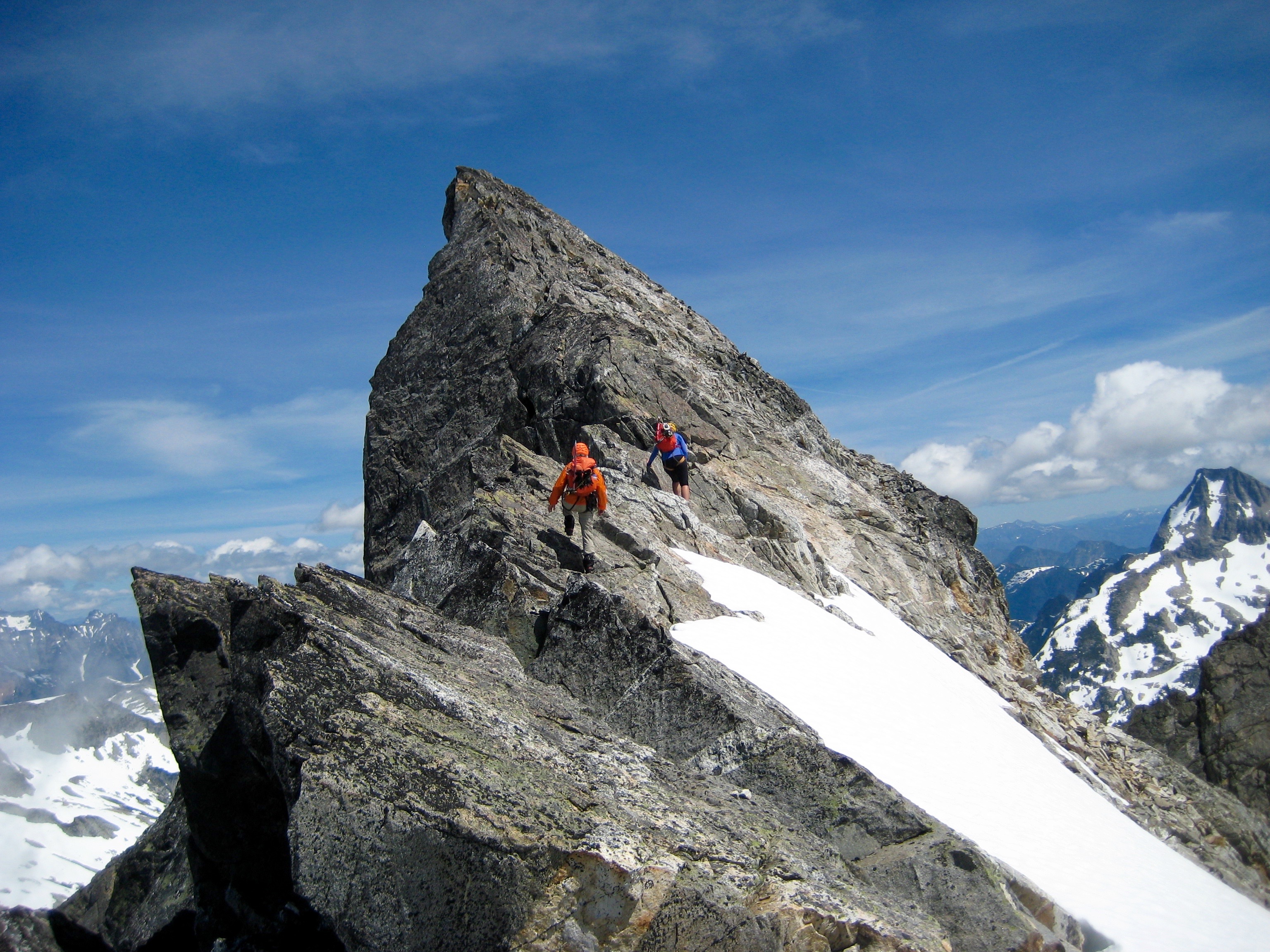 Mountain climbers scrambling up the rock on the SW Ridge of Phantom Peak with linguring snow patch in the Northern Picket Range
