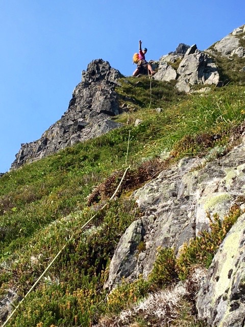 lead roped mountain climber waving from rcok outcopping above steep heather slopes on the east face of Johannesburg Mountain in the North Cascades Mountains