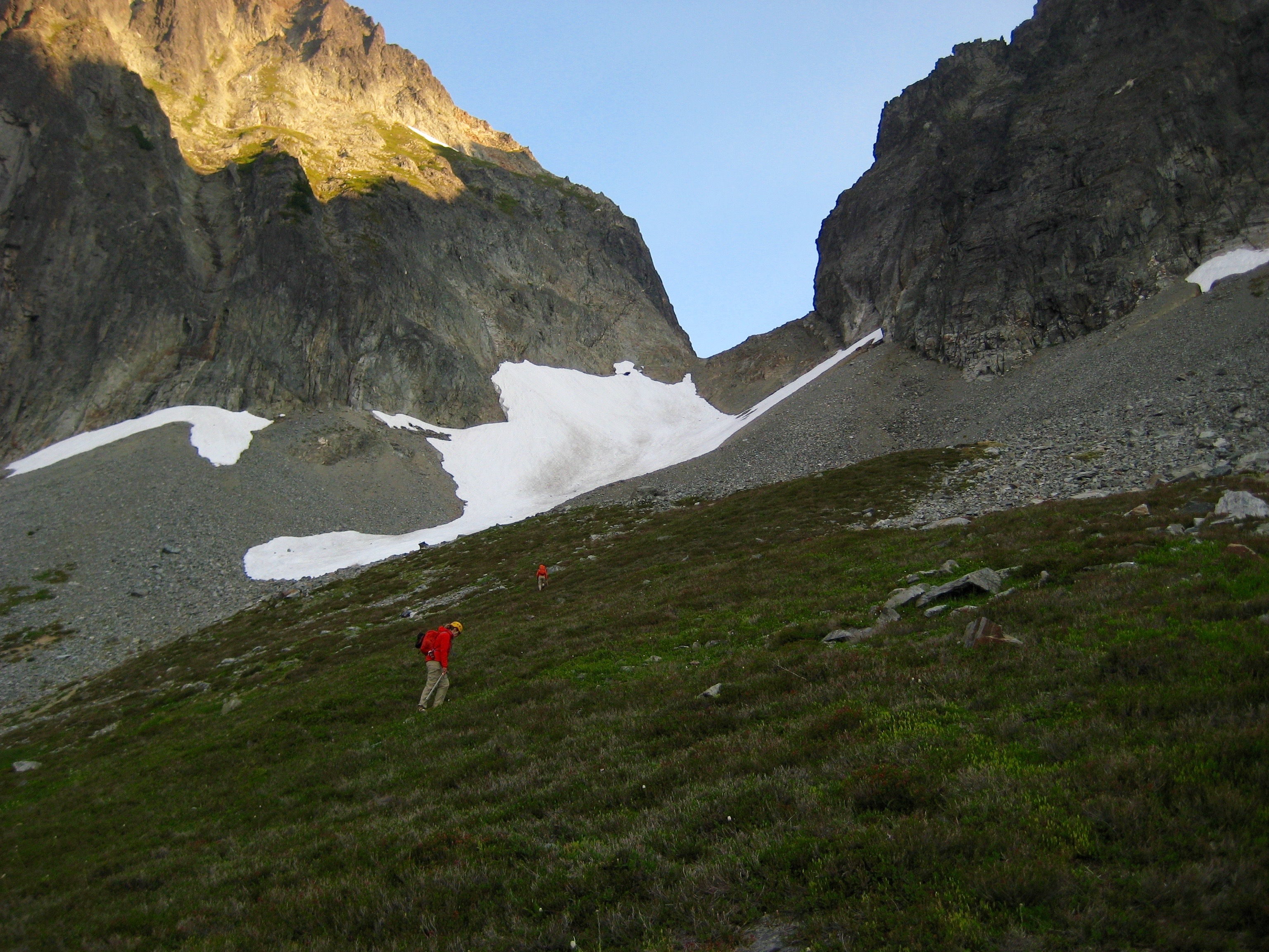 mountain climbers ascending heather towards scree slopes and a snow patch below Johannesburg Mountain in North Cascades National Park