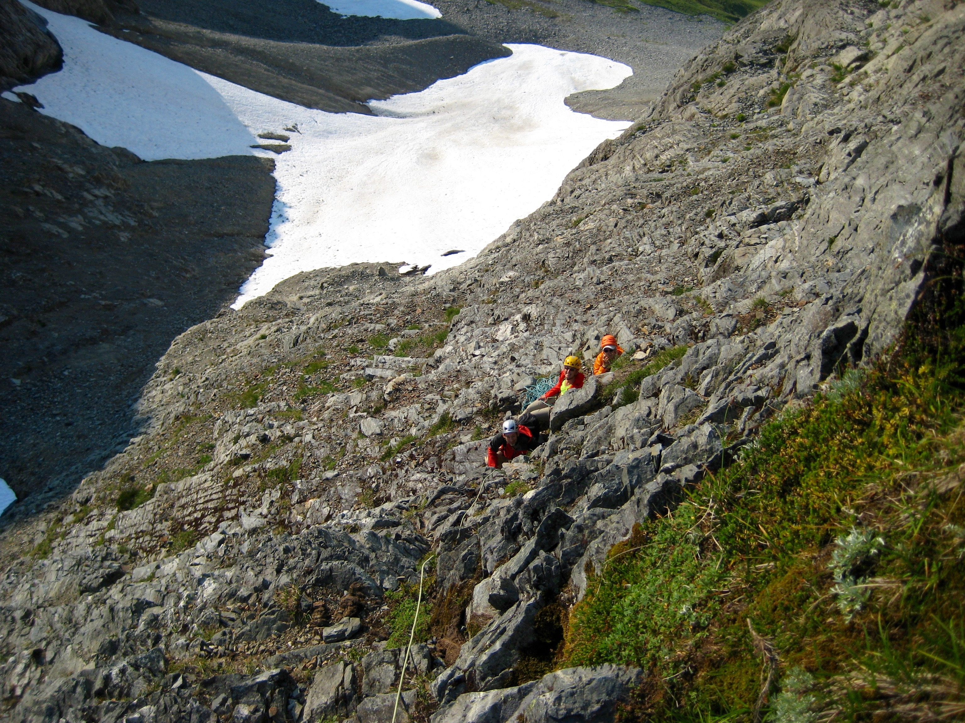 looking down at mountain climbers belaying under the rock cliffs with snow fields below on Johannesburg Mountain in North Cascades National Park