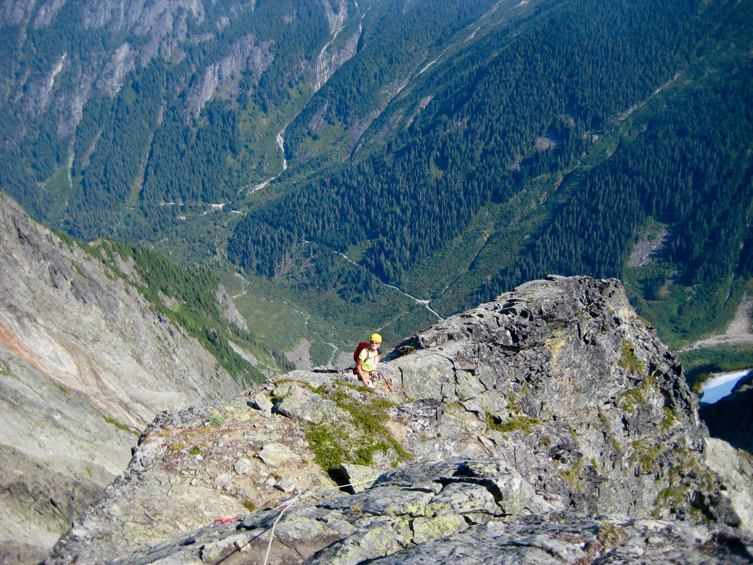 looking down at mountain climber on the steep, rocky east ridge of Johannesburg Mountain in North Cascades National Park with green valley floor far below
