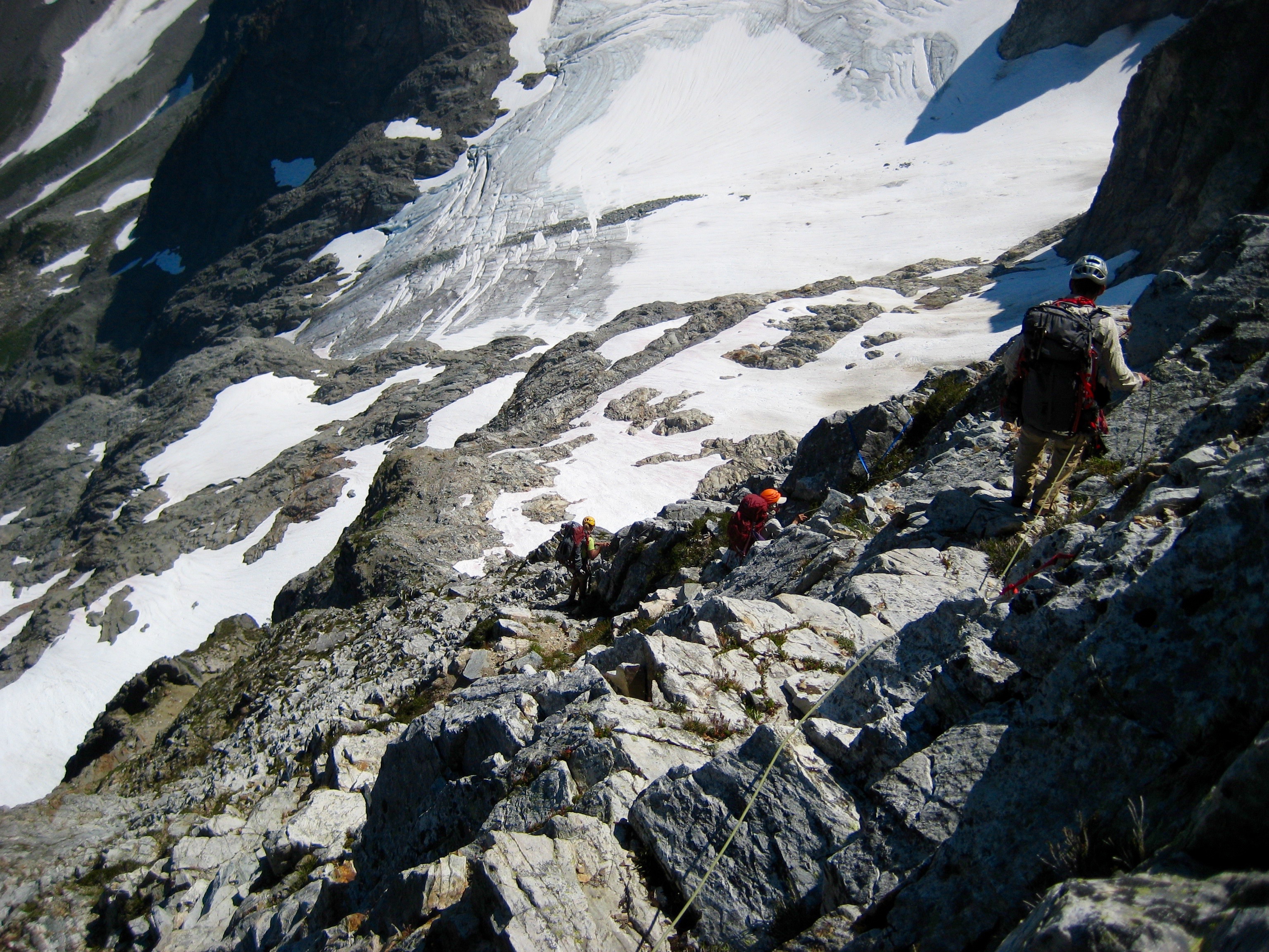 looking down on roped mountain climbers scrambling loose rocky slope below North Mixup Notch to snow slopes below 
