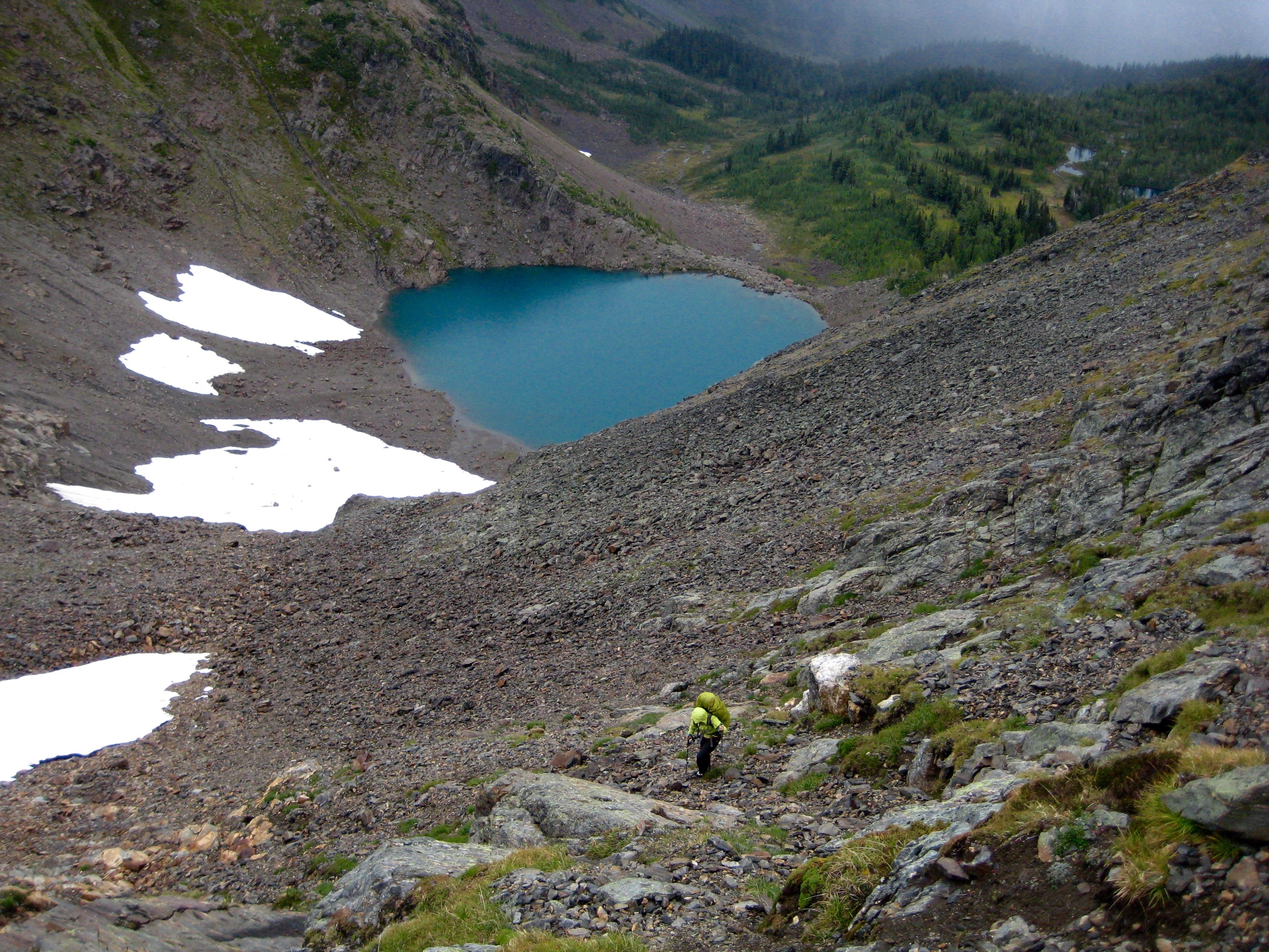 looking down on mountain climber hiking rocky scree above Cup Lake along the Chiwaukum Traverse with snow patches in the Alpine Lakes Wilderness