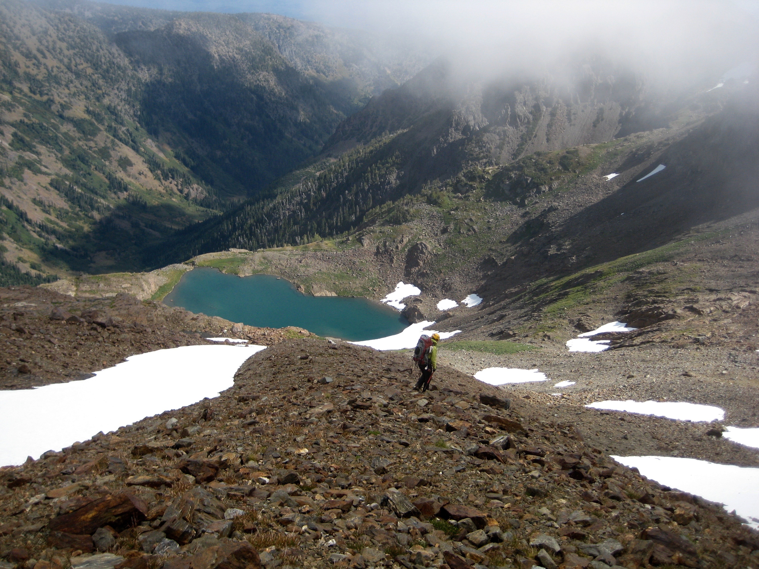 mountain climber traversing scree field with linguring snow patches above Lake Charles along the Chiwaukum Traverse in the Alpine Lakes Wilderness