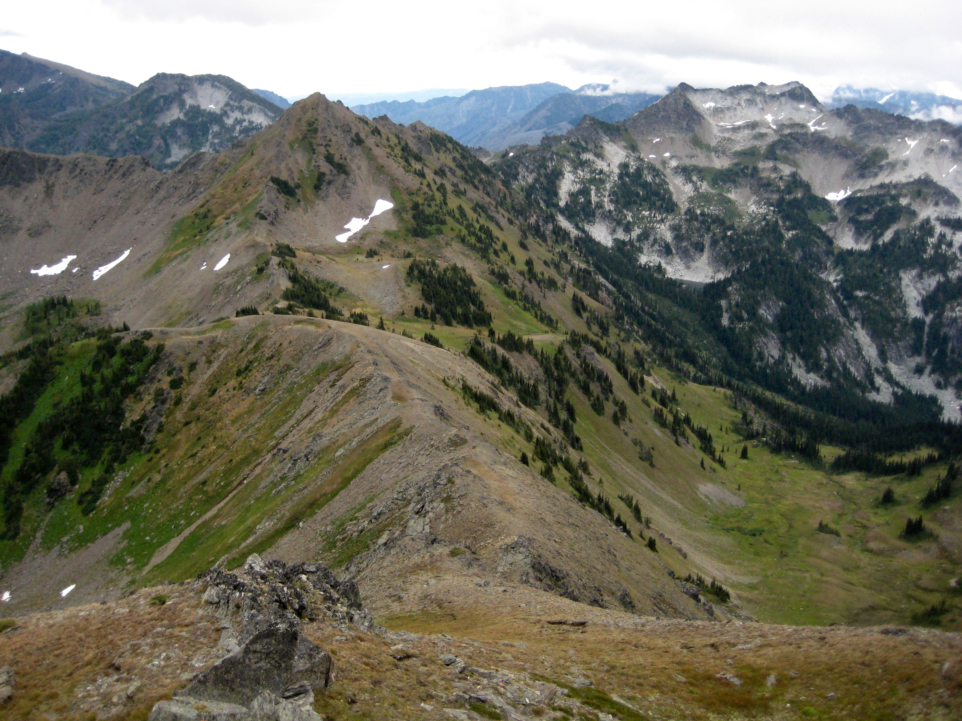 Ladies Pass down a long grassy ridge as seen from Ladies Peak along the Chiwaukum Traverse with the Alpine Lakes Wilderness in the background