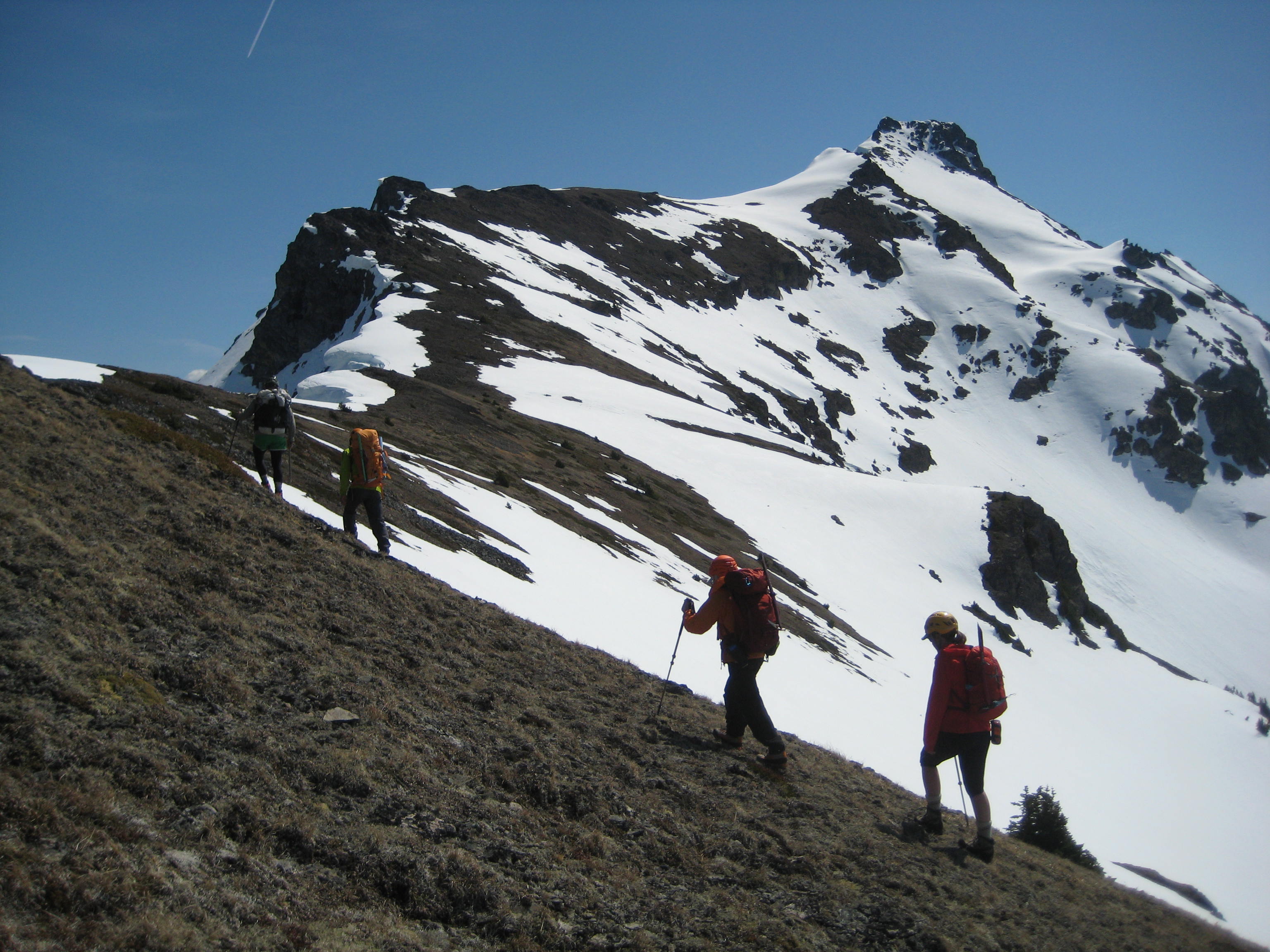 mountain climbers hiking up to the barren ridge with Silvertip Mountain in the background