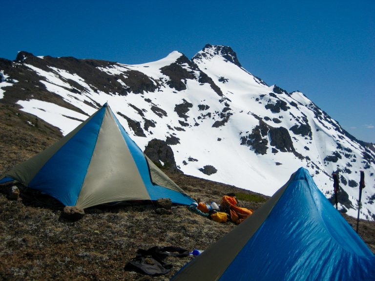 mountain climber tents sit on a barren ridge crest below snow-covered Silvertip Mountain in the Sumallo Mountains of BC Canada