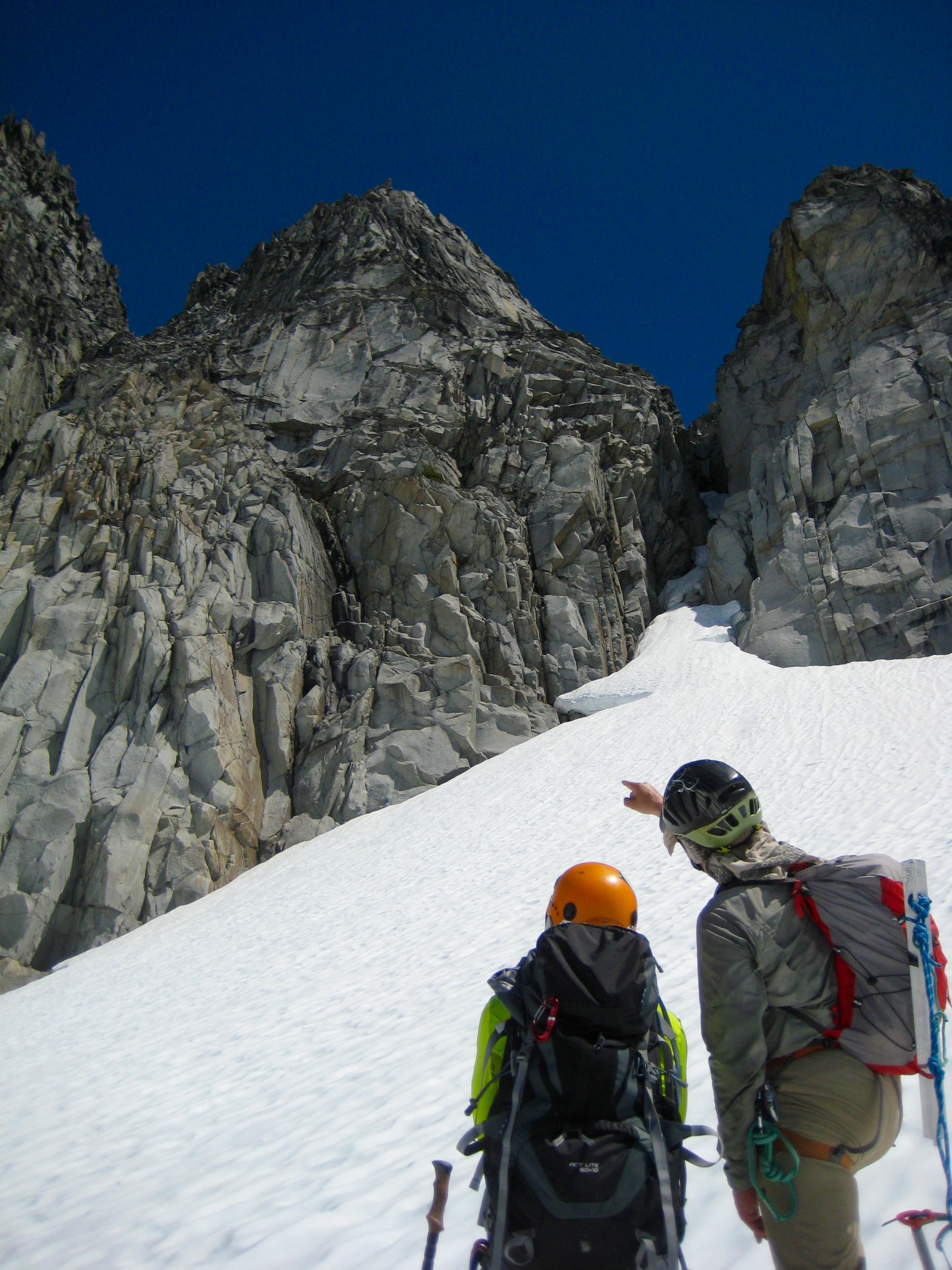 mountain climbers looking up snow fields towards steep rock assessing climbing route on Gunsight Peak in the Glacier Peak WIlderness
