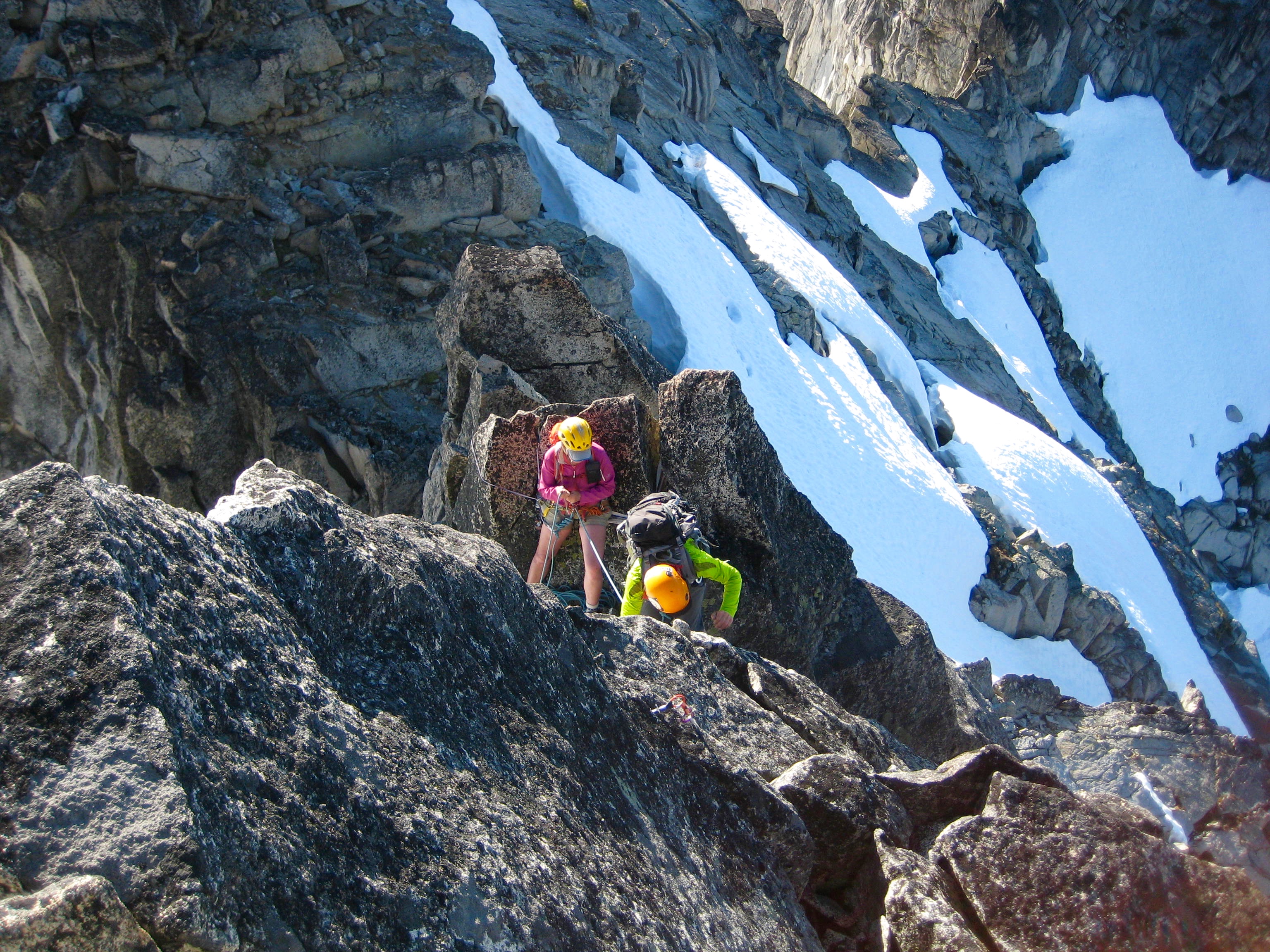 looking down on mountain climbers rappelling the ridge crest of Gunsight Peak with snow patches in the background
