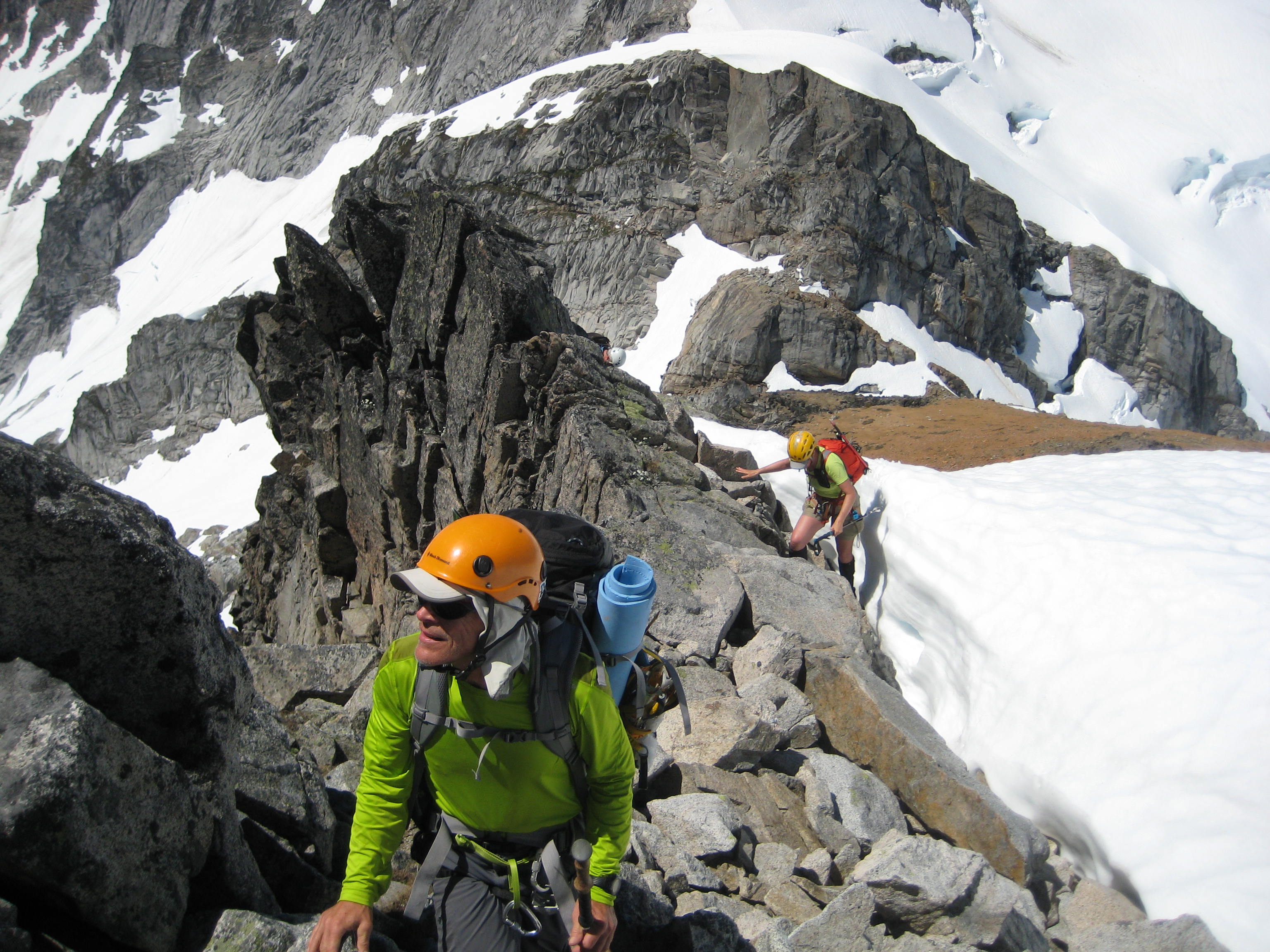 mountain climbers scrambling rock ridge next to snow slope on the upper west ridge of Sinister Peak in the Ptarmigan Mountains 