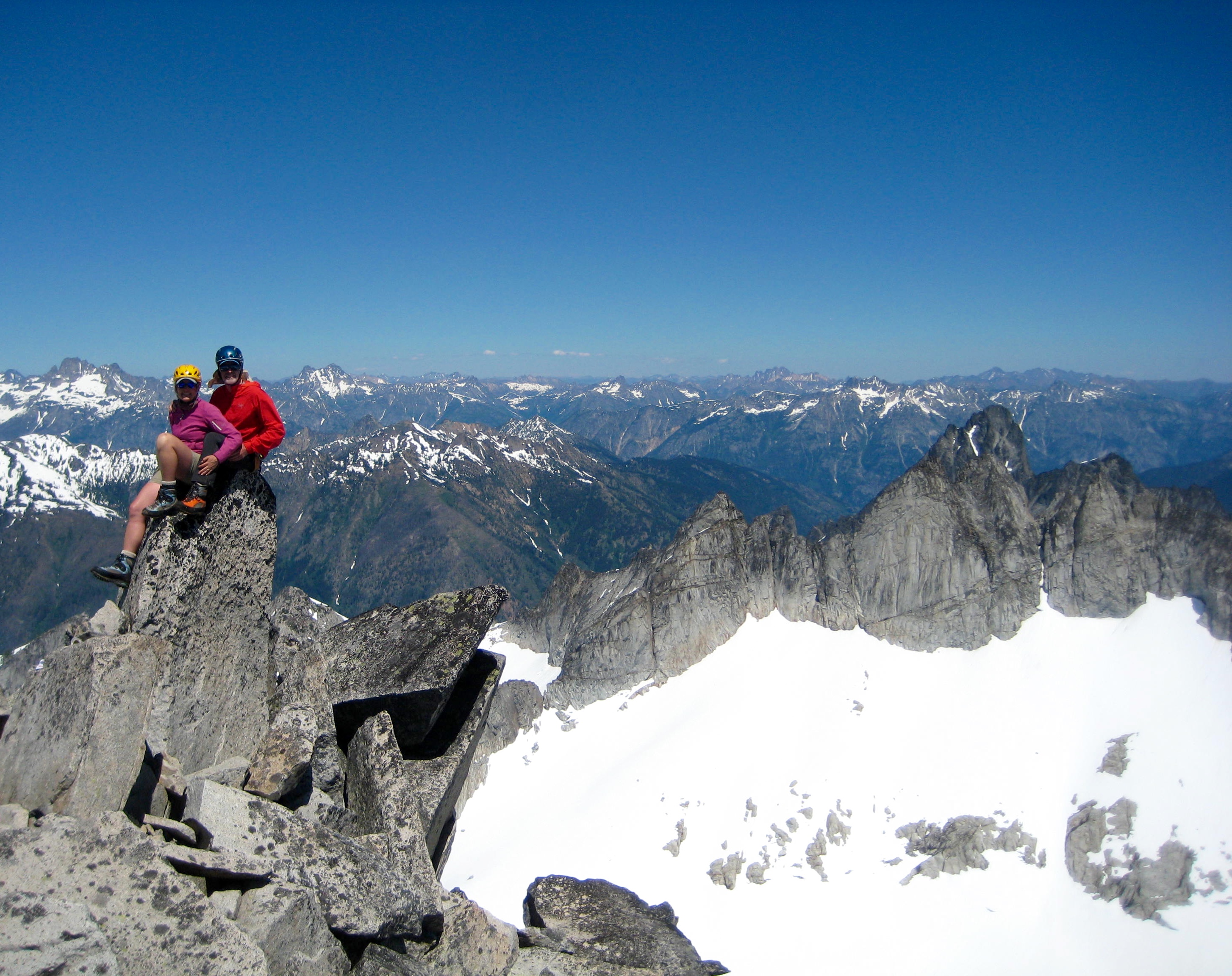 mountain climbers sitting on the rock horn summit of Sinister Peak with the Ptarmigan Mountains in the background