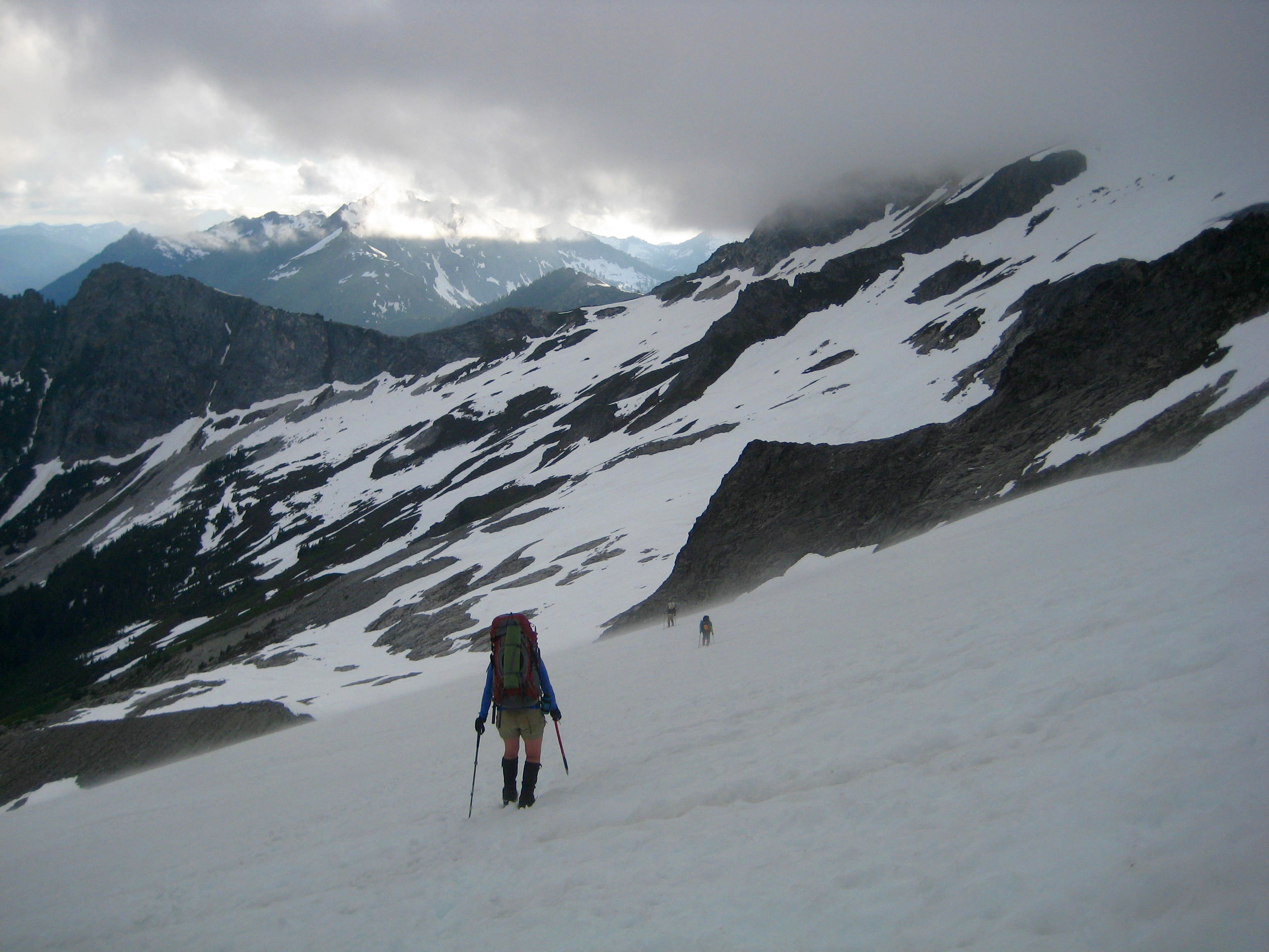 mountain climbers descending snow slopes in the Ptarmigan Mountains with grey clouds overhead