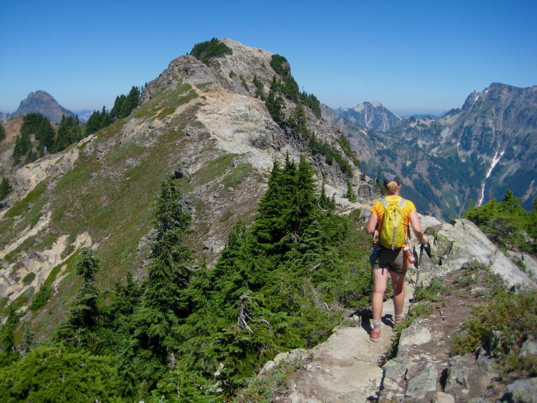 A solo hiker follows a narrow ridge crest toward Alta Mountain summit