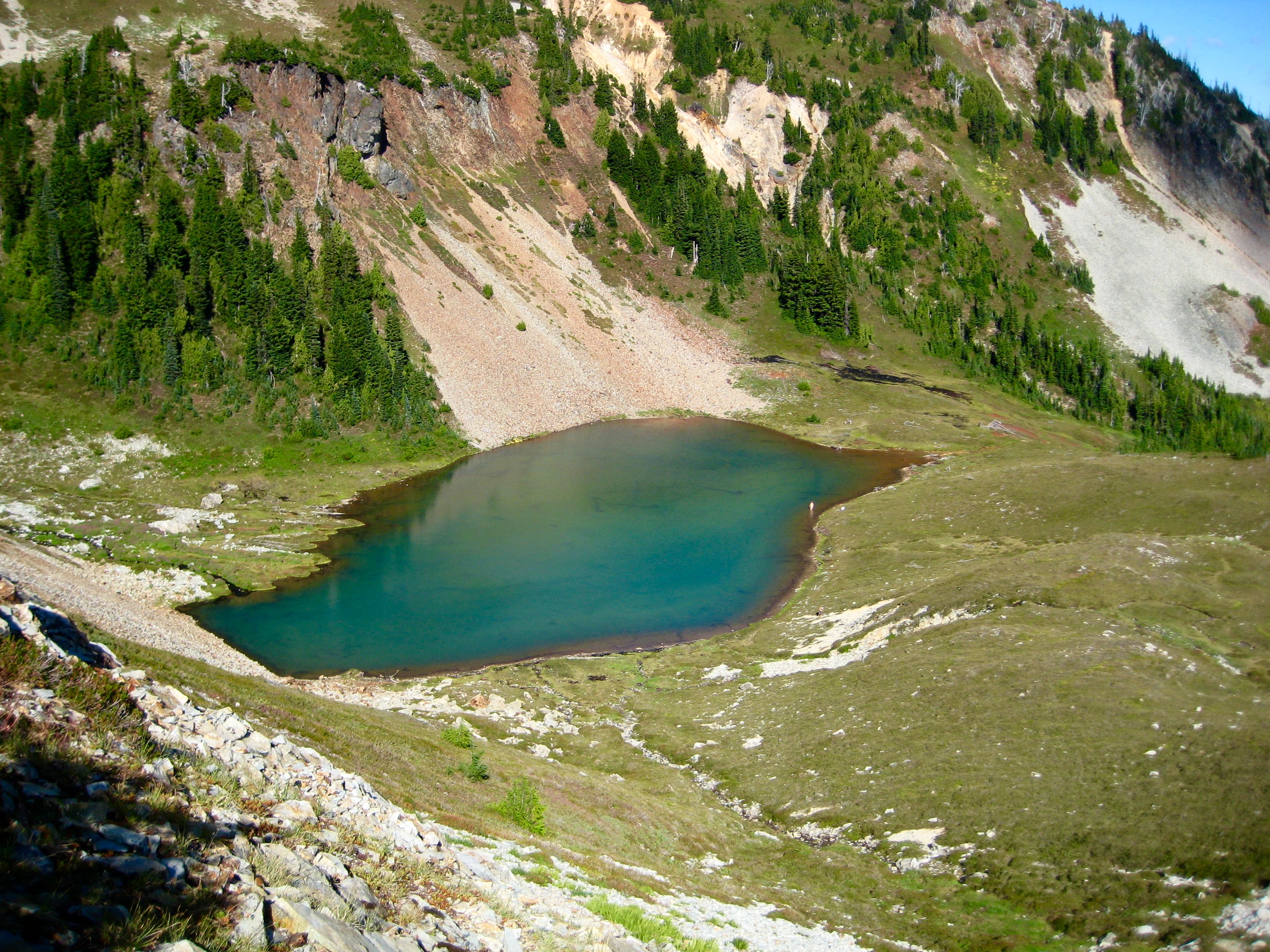Lower Middle Lake in a grassy meadow with colorful rock shoreline in the American Chilliwack Mountains