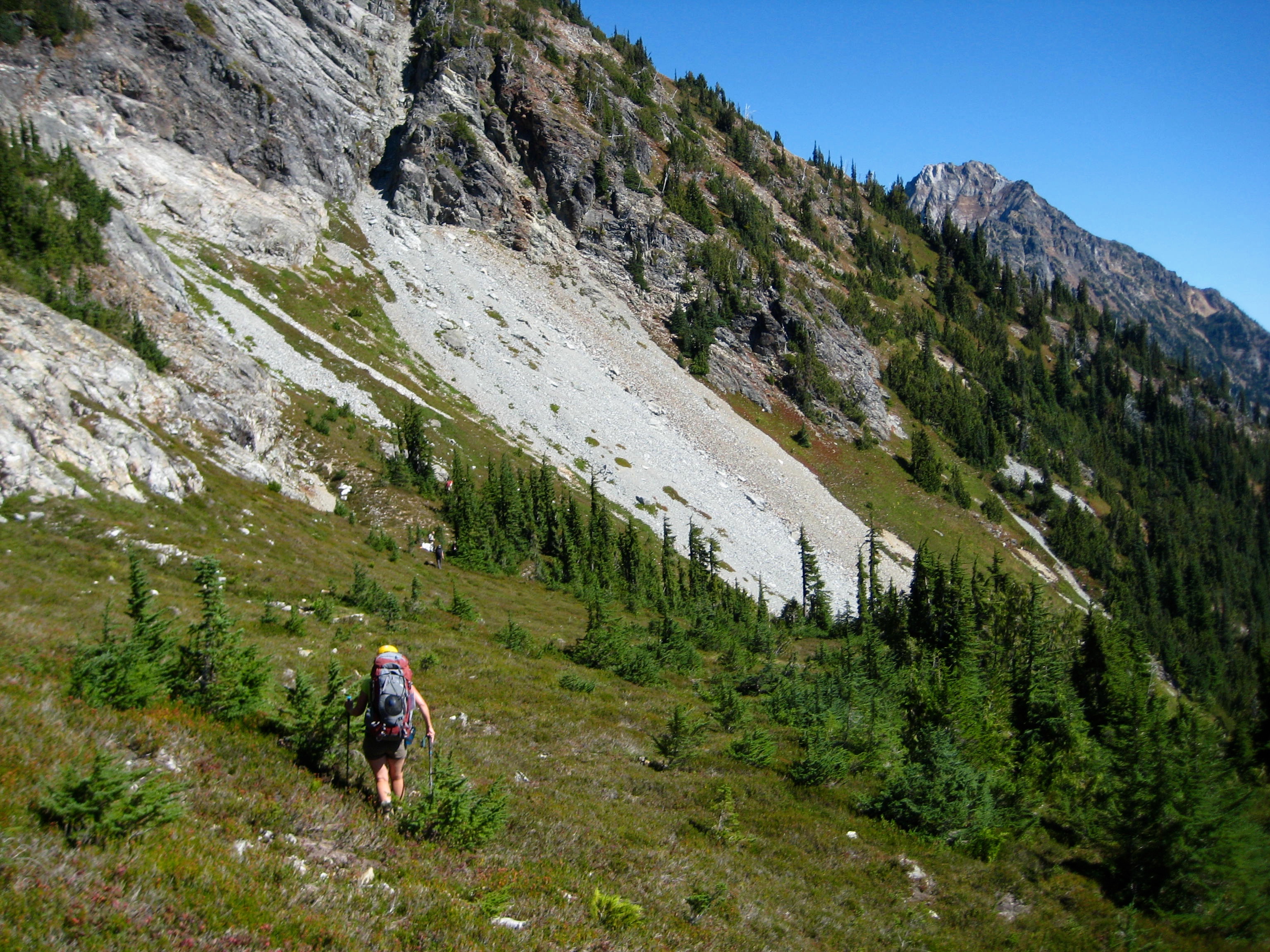 mountain climber traversing alpine slope below rocky slabs in the American Chilliwack Mountains