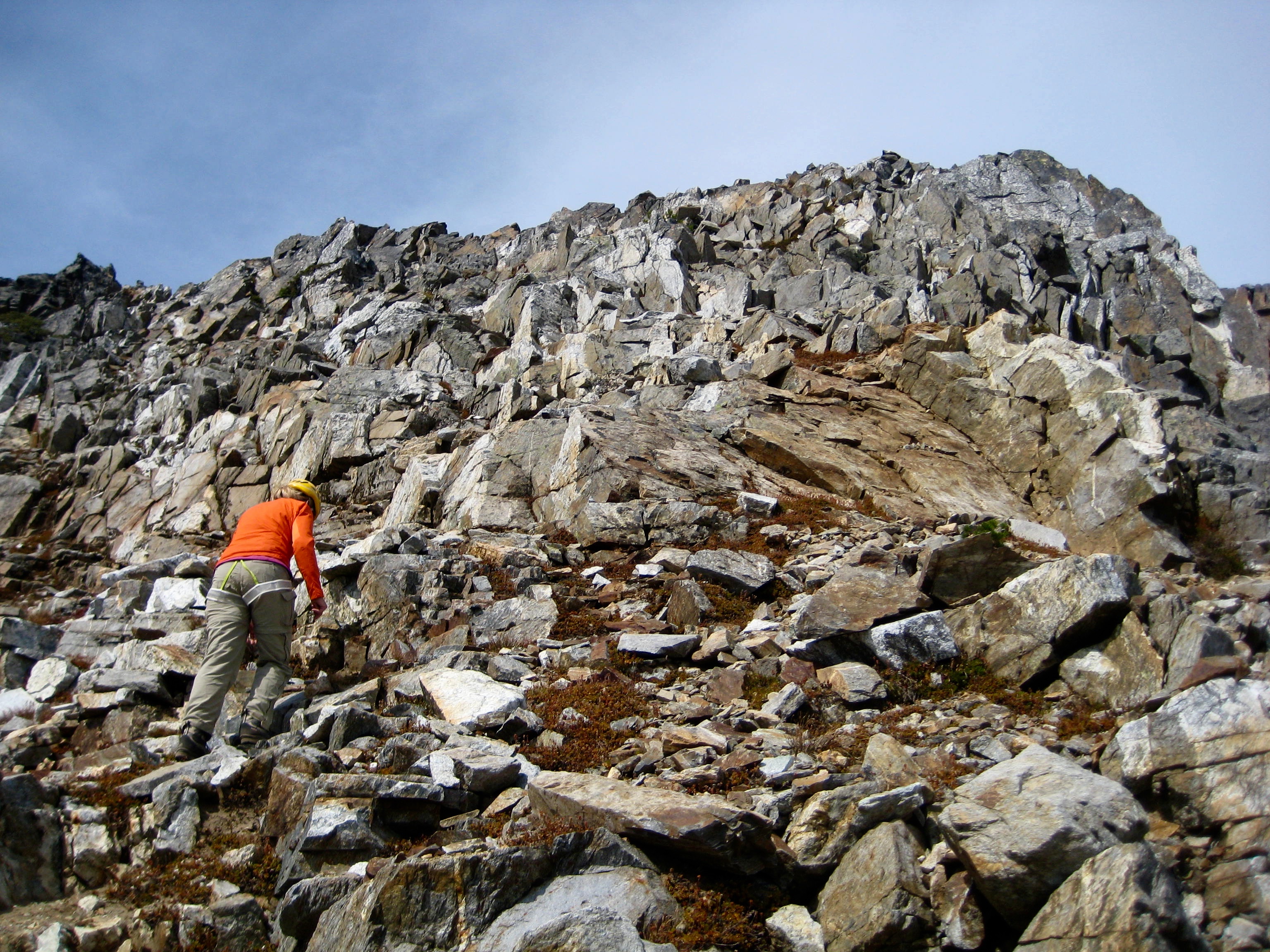 mountain climber scrambling up loose rock towards the summit of Sitting Bull Mountain in the Glacier Peak Wilderness