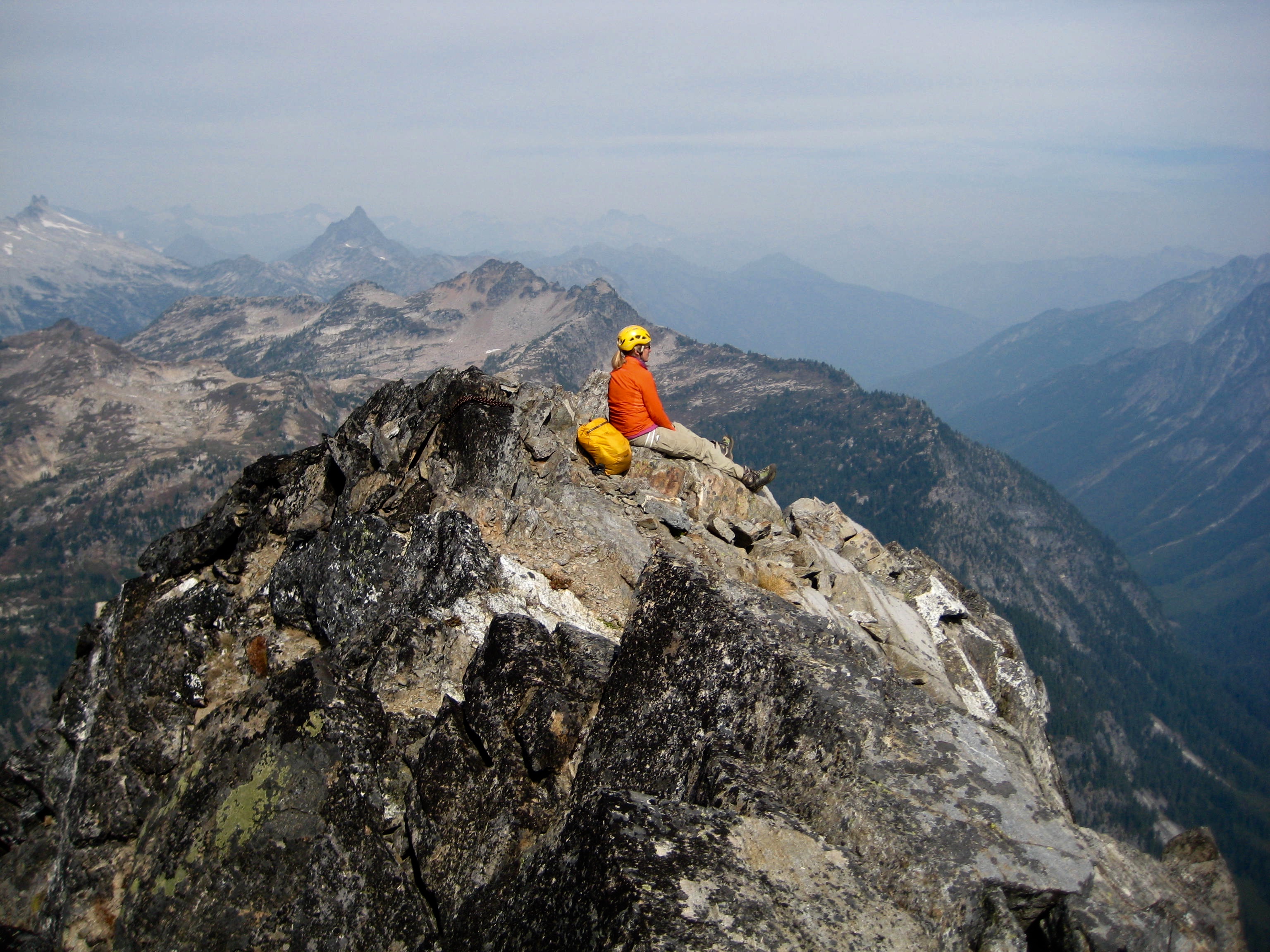 mountain climber sitting on the summit of Sitting Bull Mountain with Anges Mountain in the distance through the smoky air