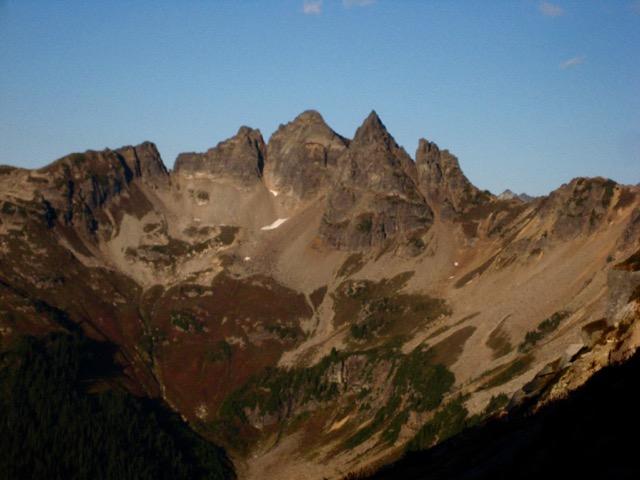 multiple rock pinnacles of Sitting Bull Mountain stand on a ridge above green heather meadows in the Glacier Peak Wilderness