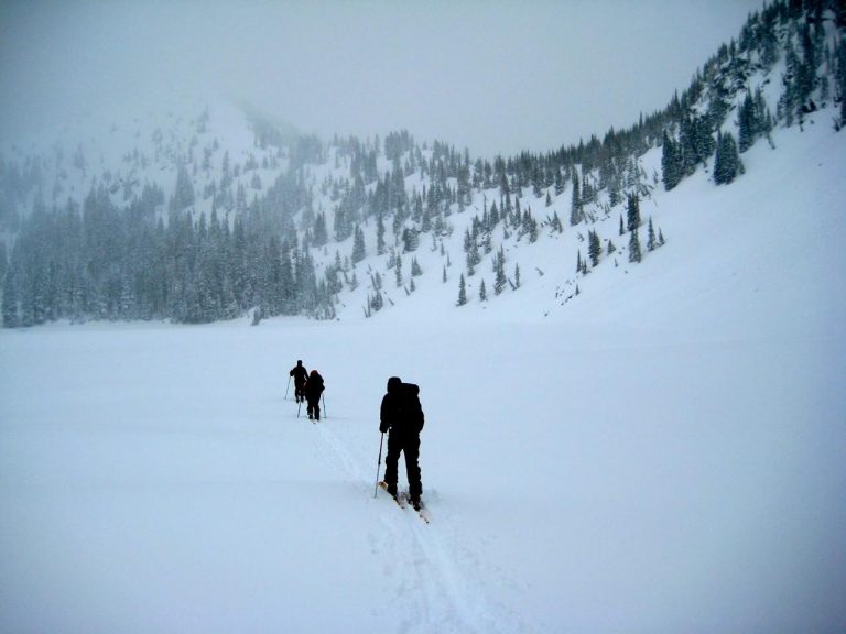 Backcountry skiers cross a frozen lake on a foggy day