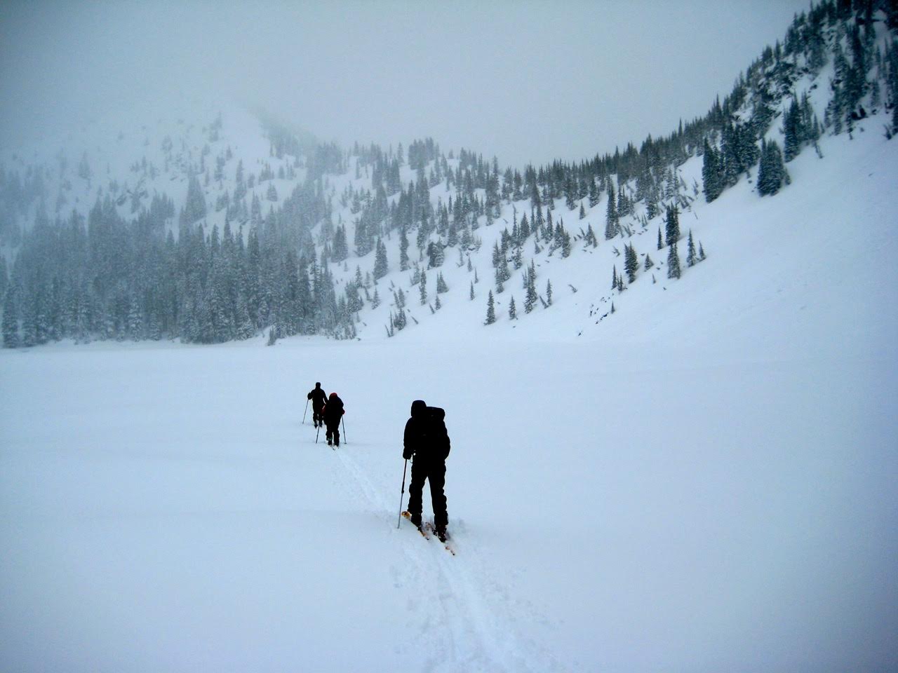 Backcountry skiers cross a frozen lake on a foggy day