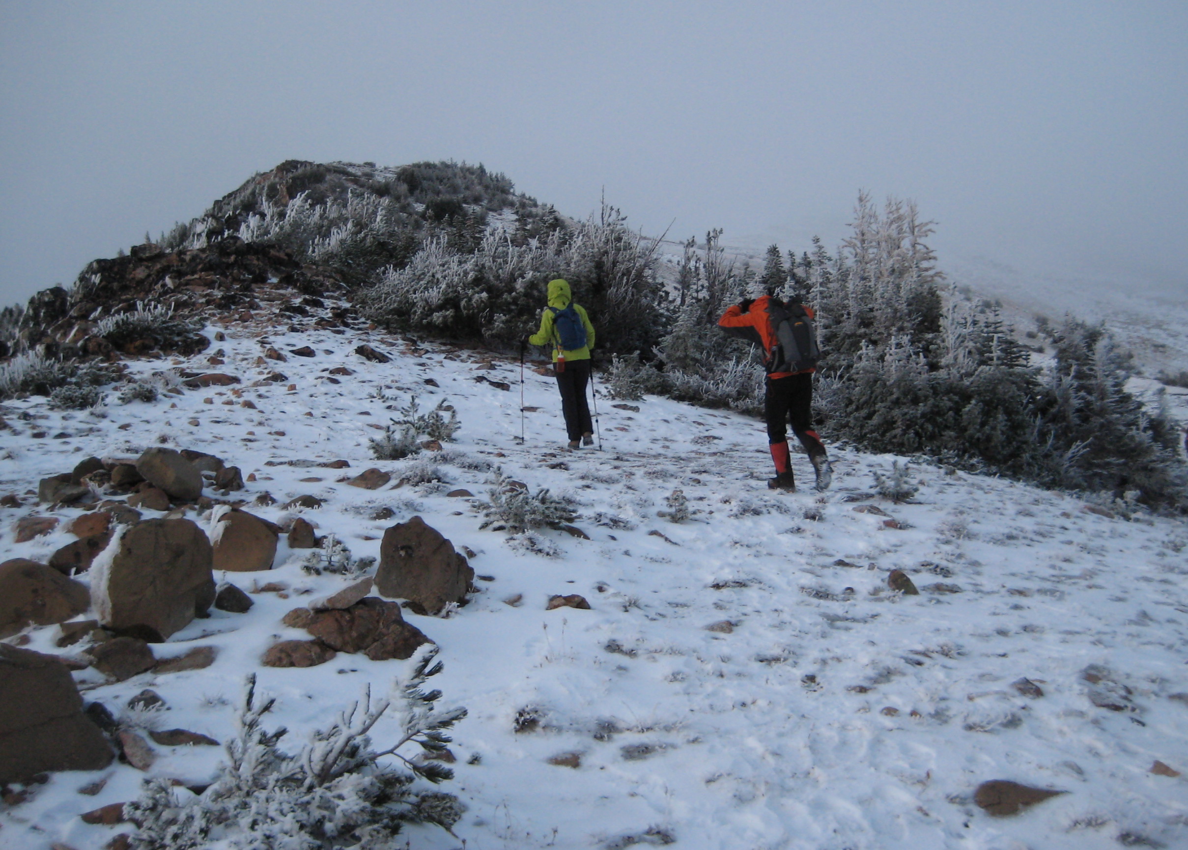 Two people hike up a snowy ridge toward Victoria Point