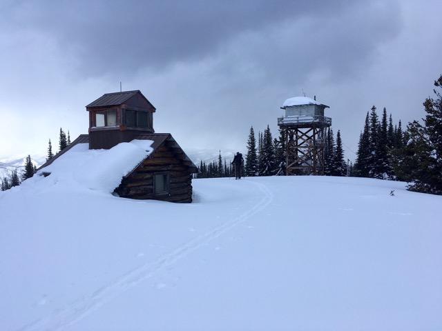 Two wooden cabins of different eras stand at Monument 83 Lookout in the snow at the US-Canadian Border