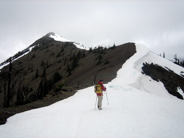 A climber walks up a snow-covered ridge crest toward Freedom Peak summit
