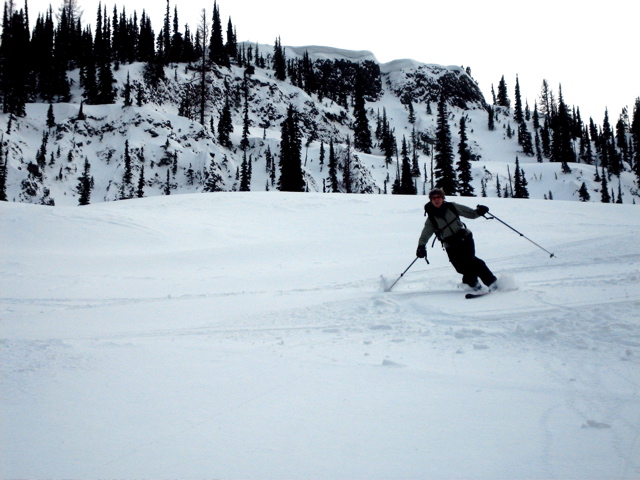 A telemark skiers carves a turn under a rocky cliff during the Tronsen Head Ski Loop