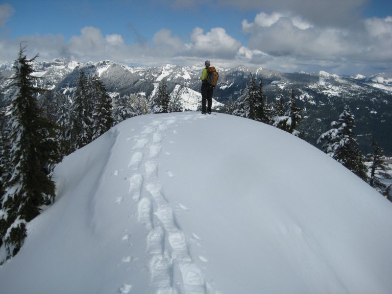 A solo snowshoer stands on the summit of Mt Catherine in the Iron Horse Mountains