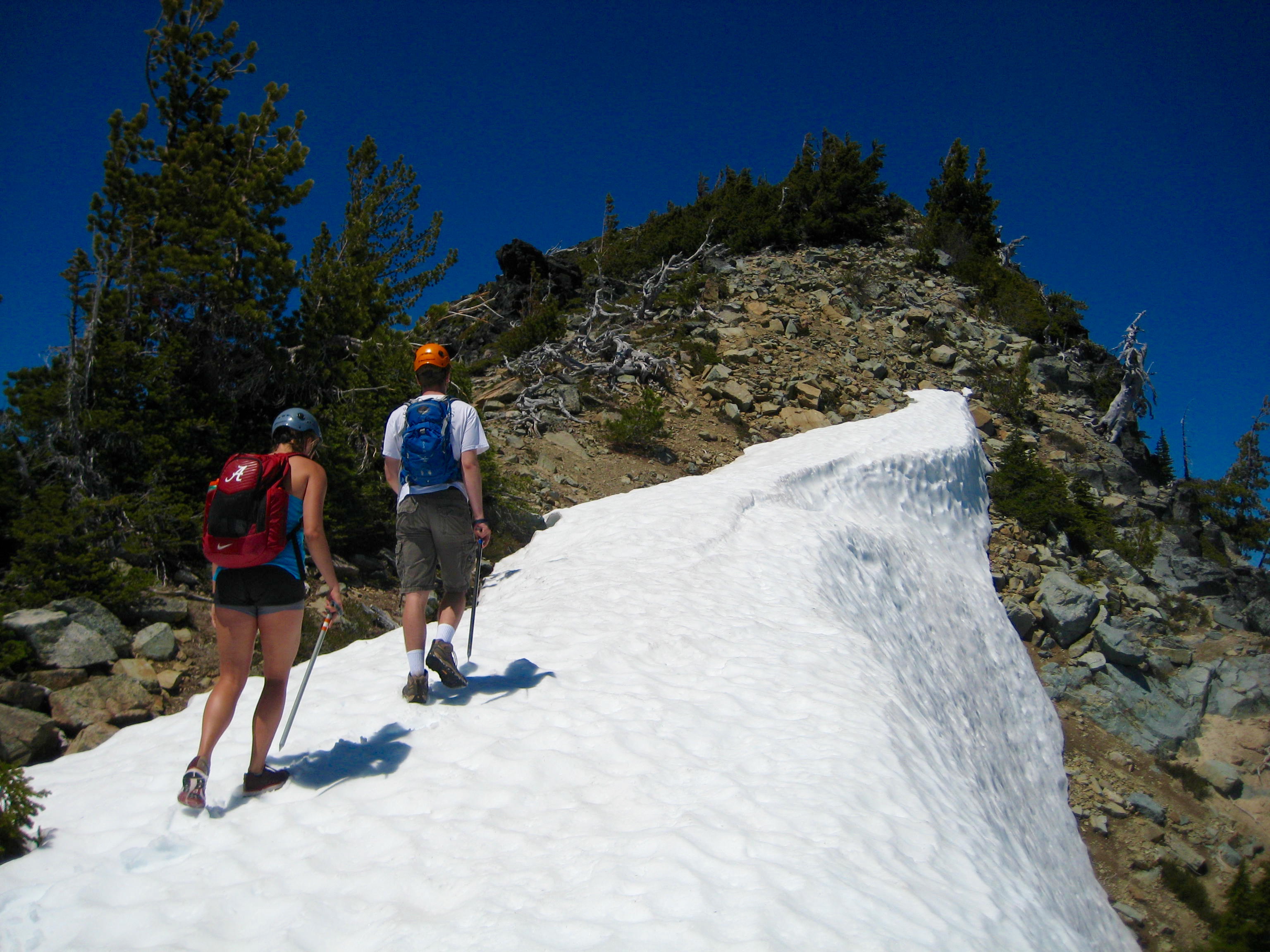 Two hikers ascend a snowy ridge on Tamanos Mountain above Owyhigh Lakes