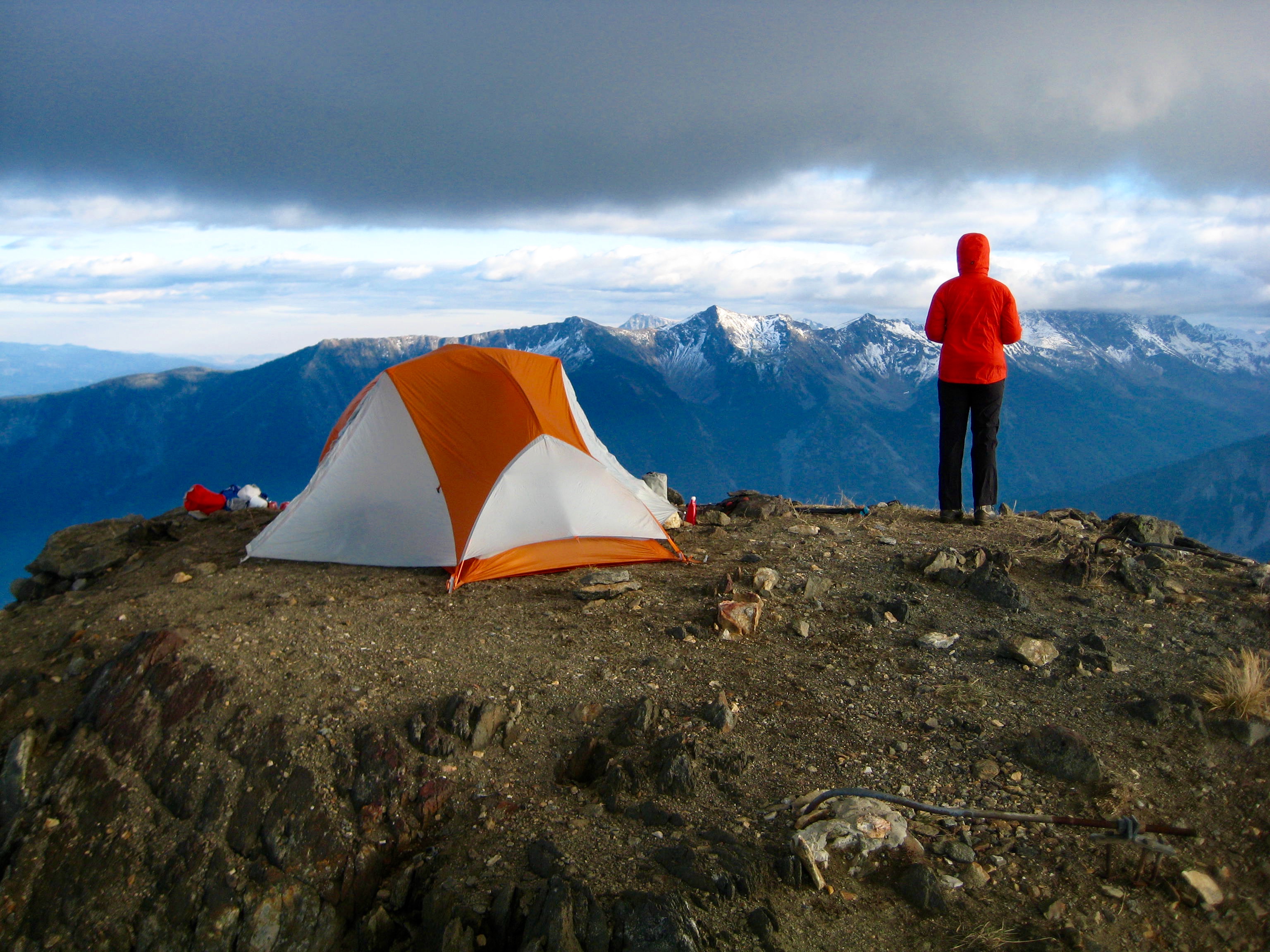 A tent and hiker stand atop the summit of Rock Mountain on Nason Ridge with dark clouds overhead
