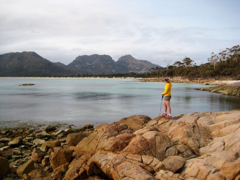 hiker stands on rock outcrops looking across Hazard Beach at Mt Mayson in Tasmania's Freycinet National Park