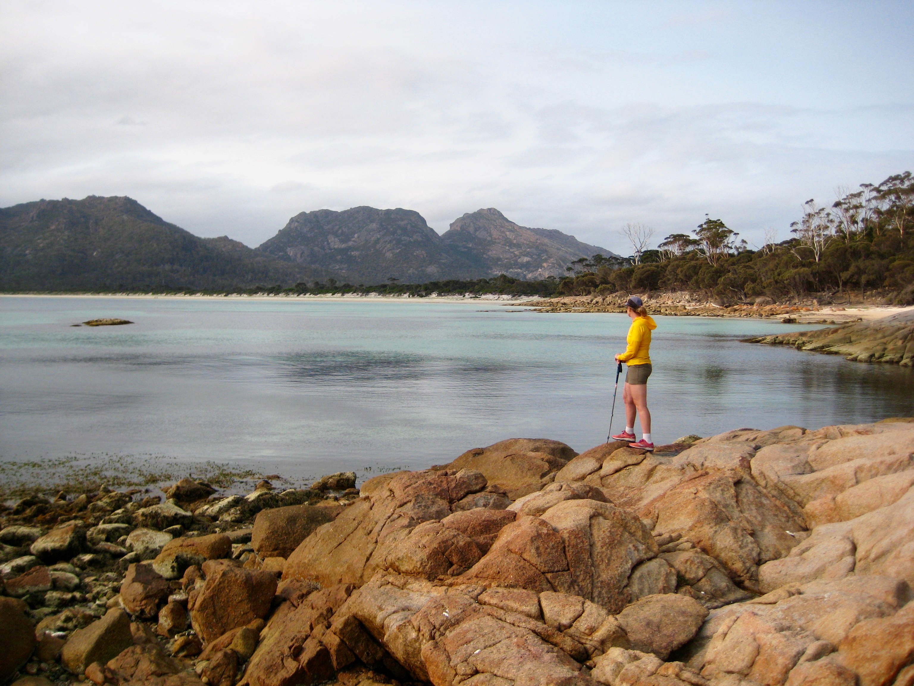 hiker stands on rock outcrops looking across Hazard Beach at Mt Mayson in Tasmania's Freycinet National Park