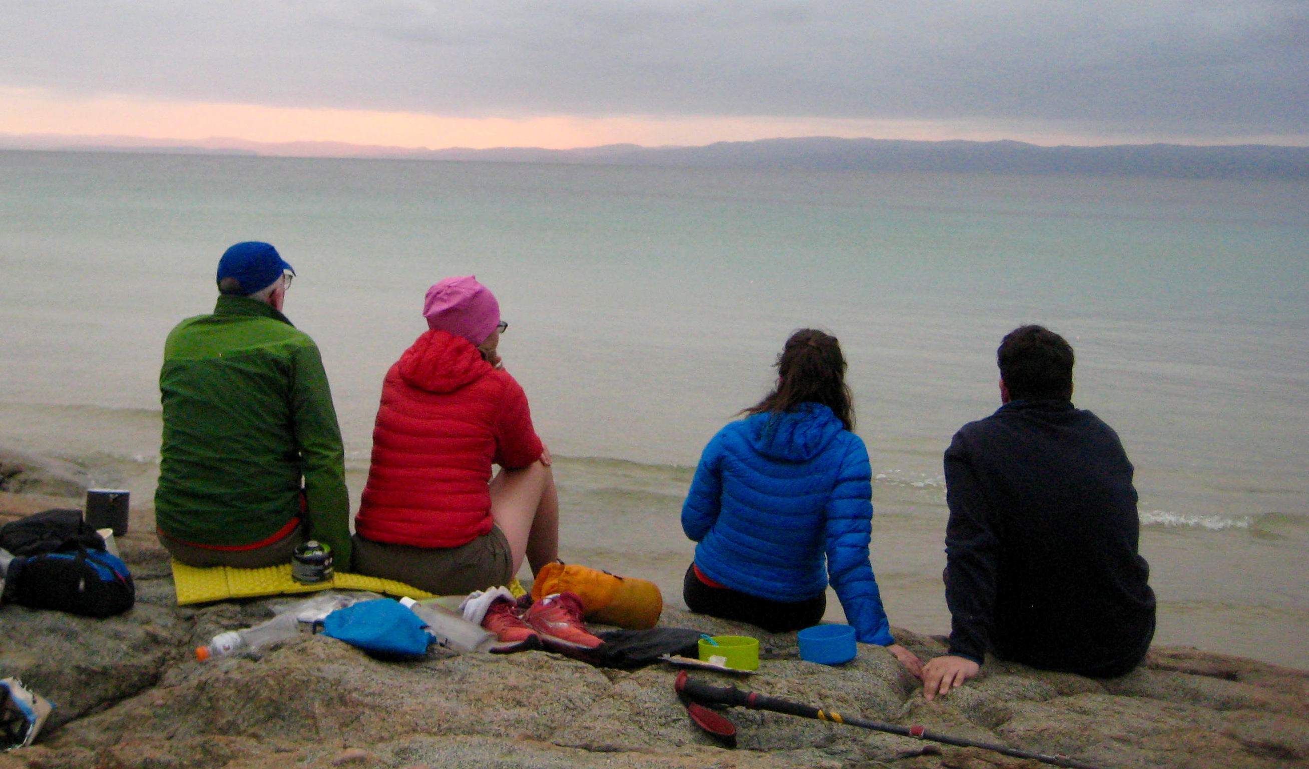 hikers sitting on rocks on Hazards Beach in Tasmania's Freycinet National Park watching the sunset over the ocean