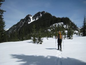 A snowshoer walks along a broad snow ridge toward Dungeon Peak