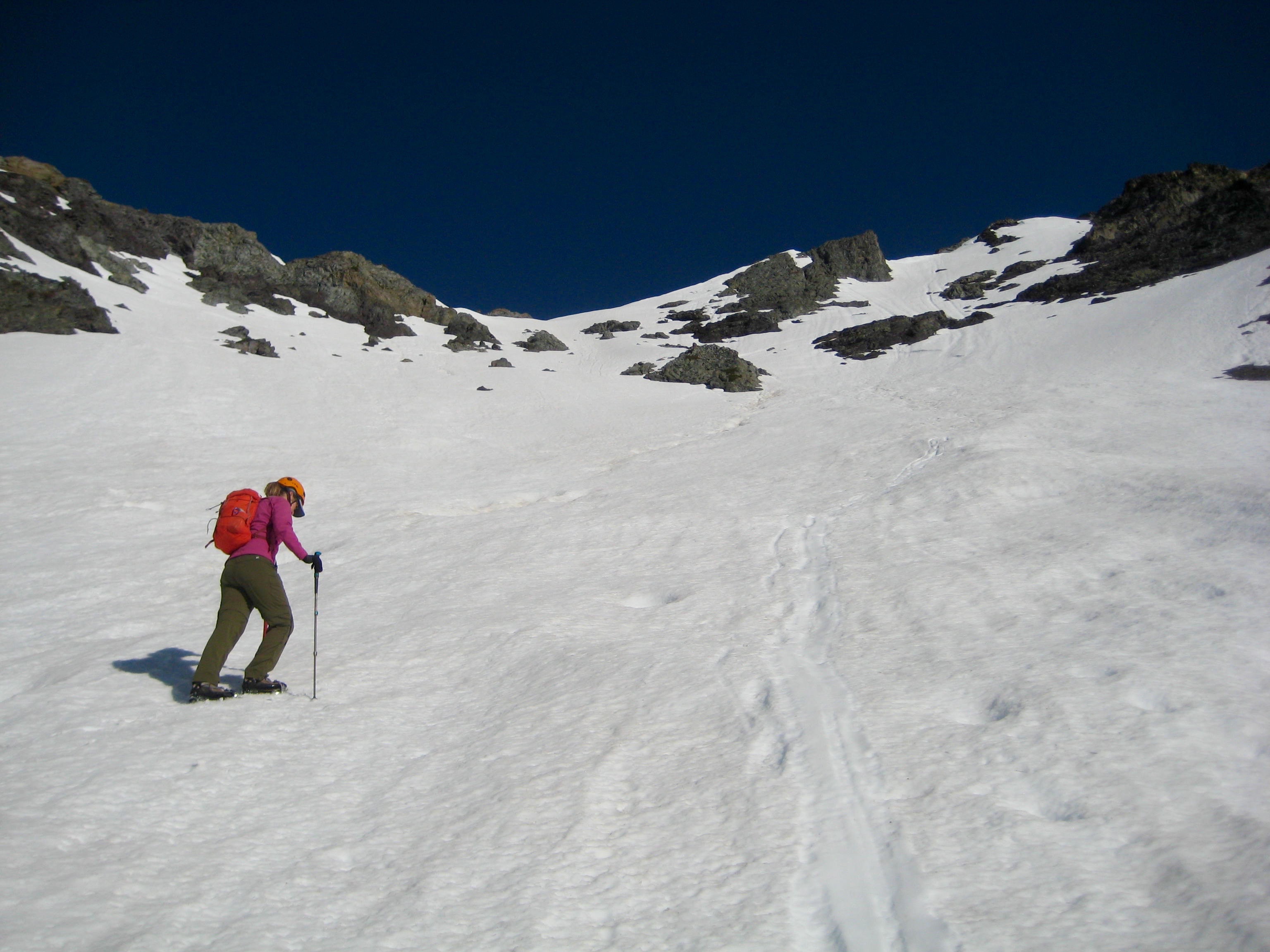 looking up at mountain climber ascending steep snow slope leading to the shoulder of Robinson Mountain in the Pasayten Wilderness