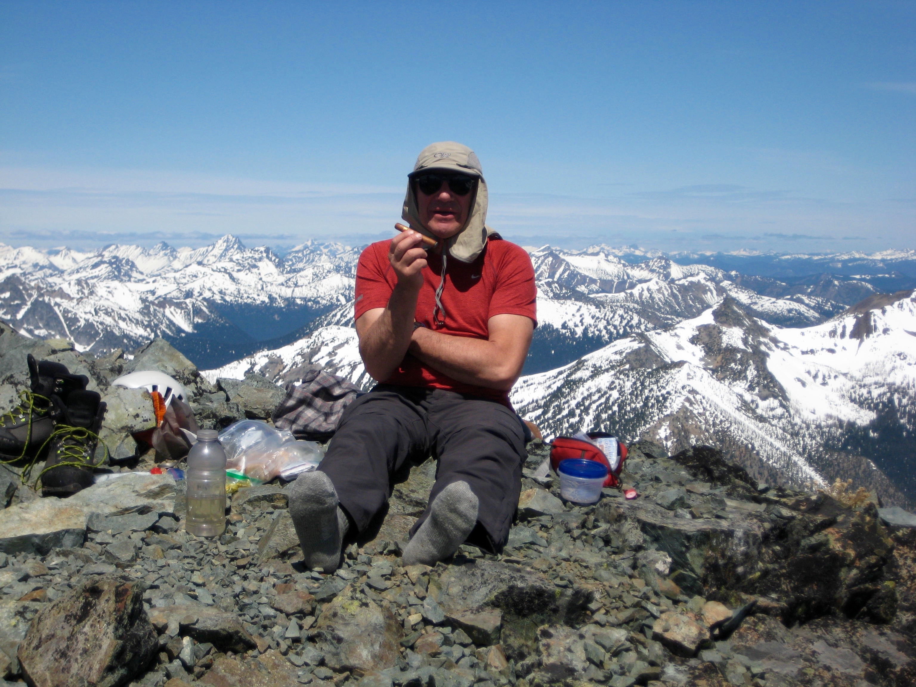 mountain climber taking a boots off break on the summit of Robinson Mountain in the Pasayten Wilderness with the snowy Glacier Peak WIlderness in the background