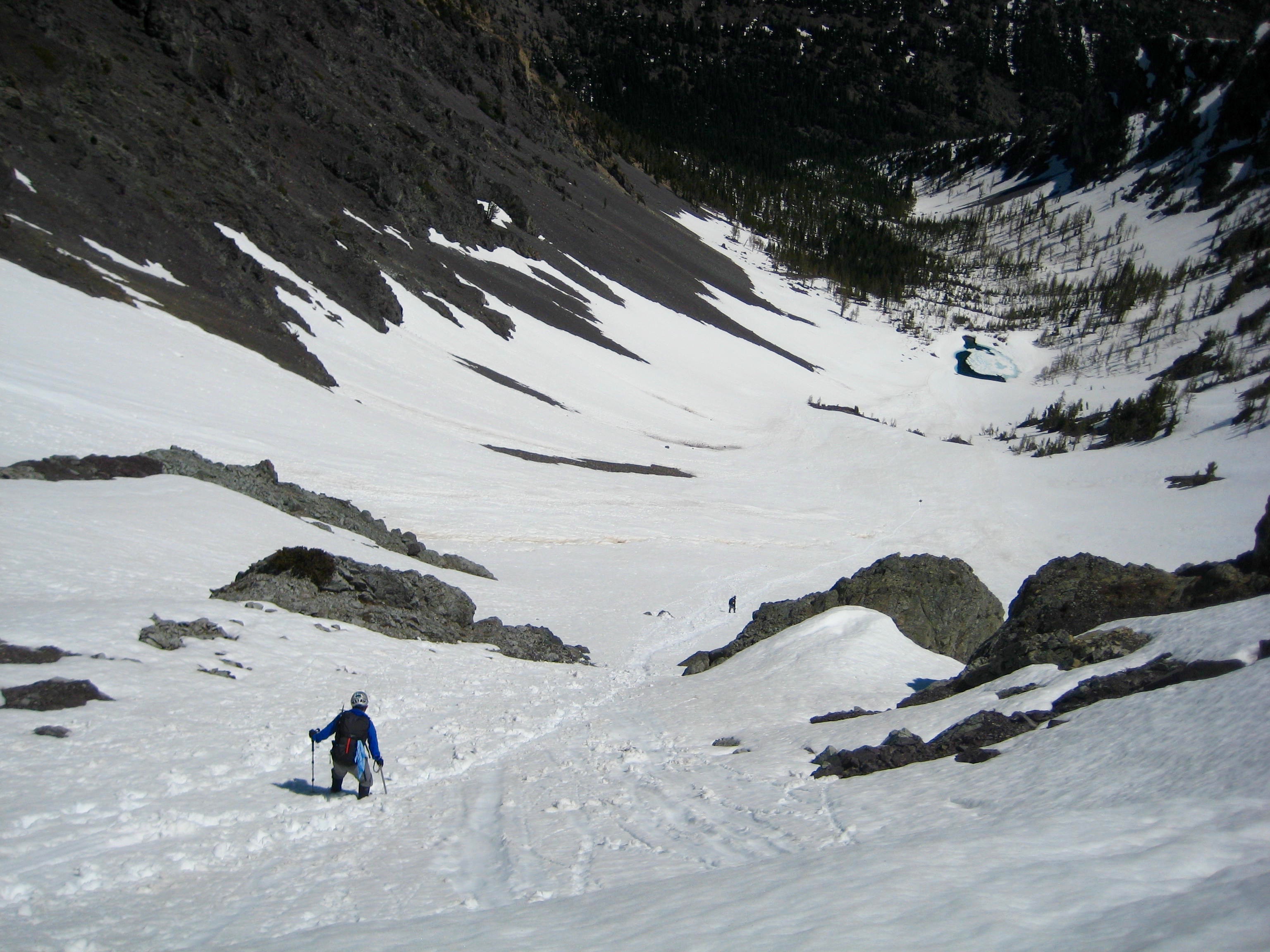 looking down on mountain climber glassading snow slope with exposed rocks leading into the basin in the Pasayten Wilderness
