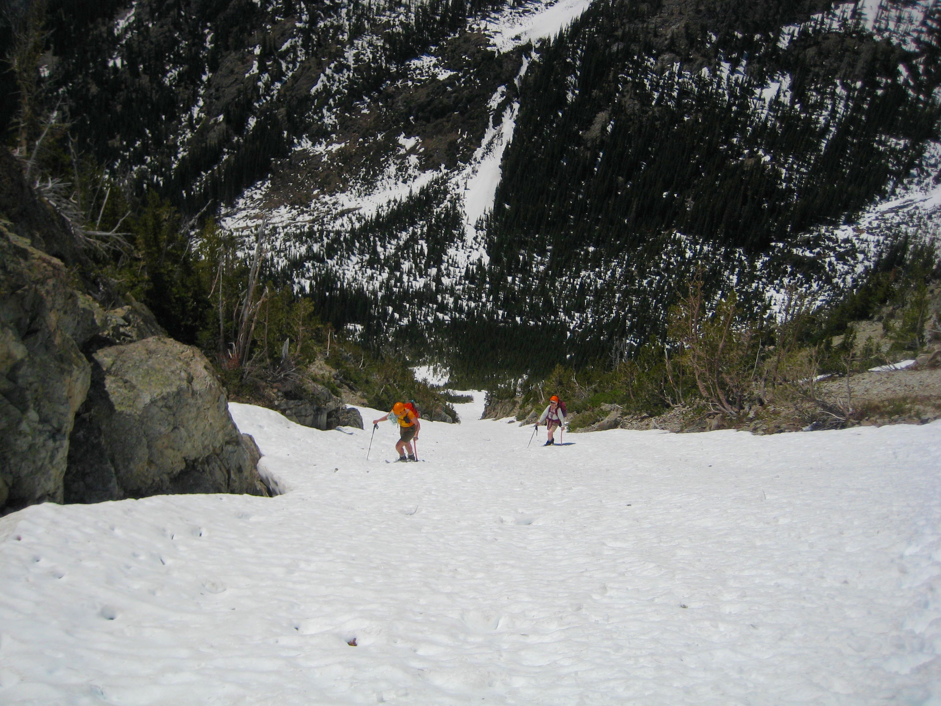 looking down on mountain climbers booting up snow chute on the shoulder of Beauty Peak in the Pasayten Wilderness with forested valley bottom below