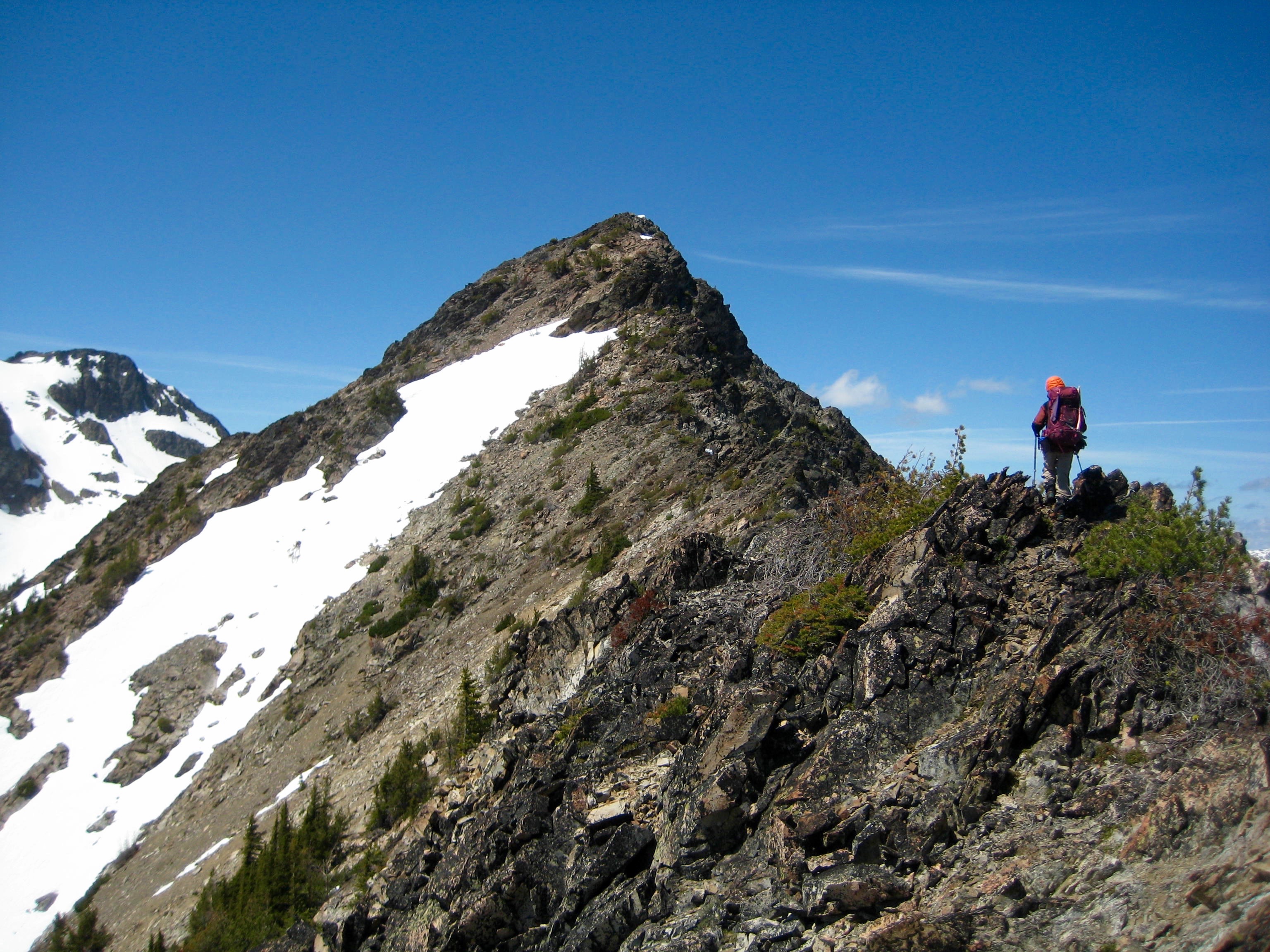 mountain climber scrambling the snow-free ridge heading to the summit of Beauty Peak in the Pasayten Wilderness with large snow field below
