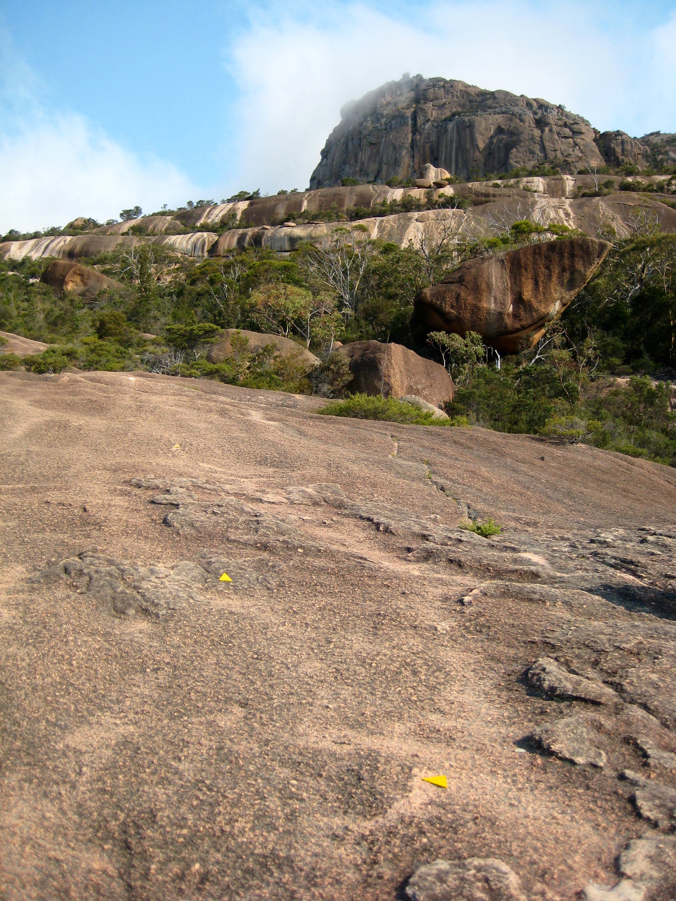 looking up large granite slab with yellow hiking trail markers leading to the summit of Mt Amoa in Tasmania's Freycinet National Park